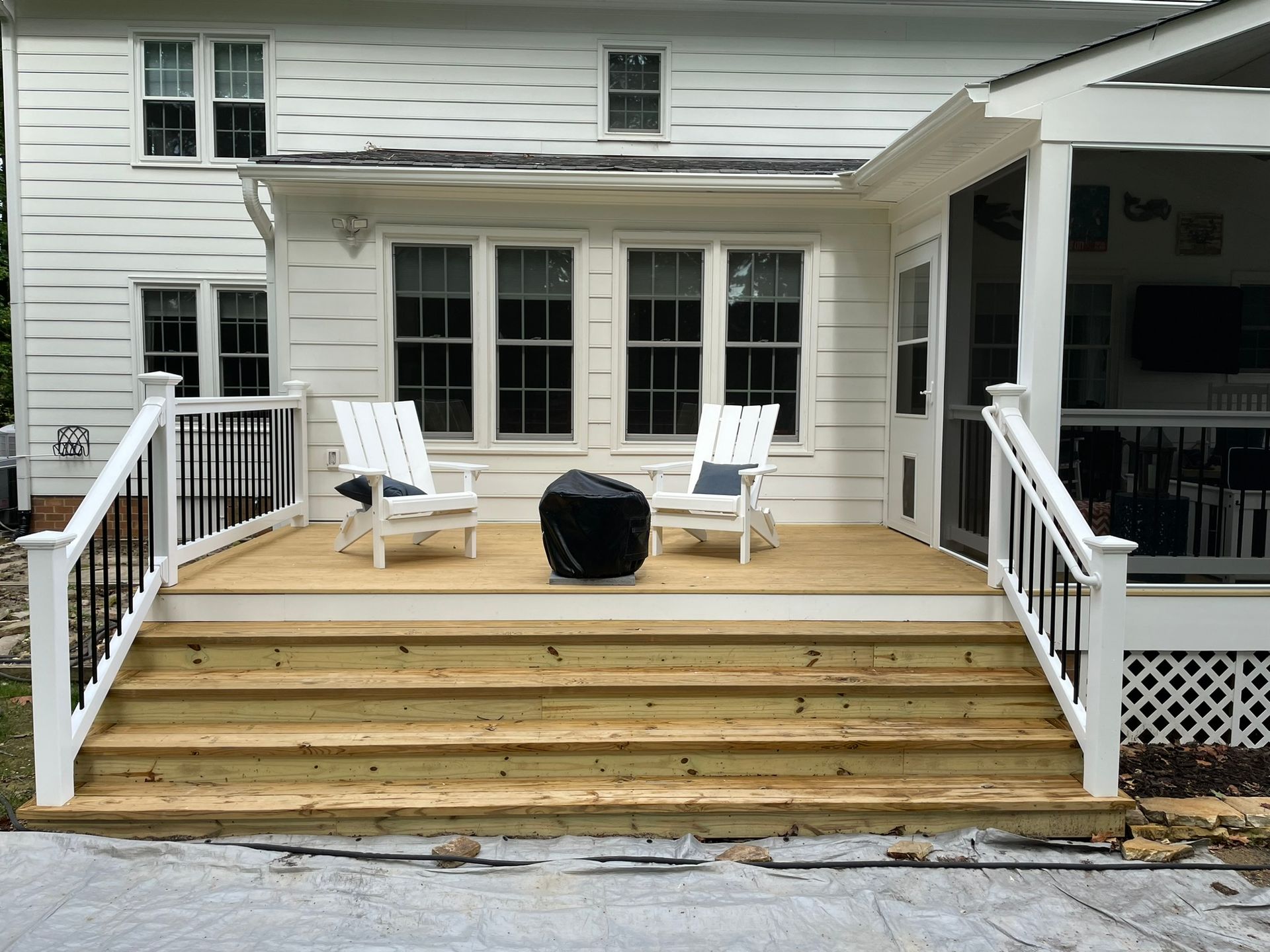 White house deck with wooden steps, three white chairs, and a black fire pit table on the patio