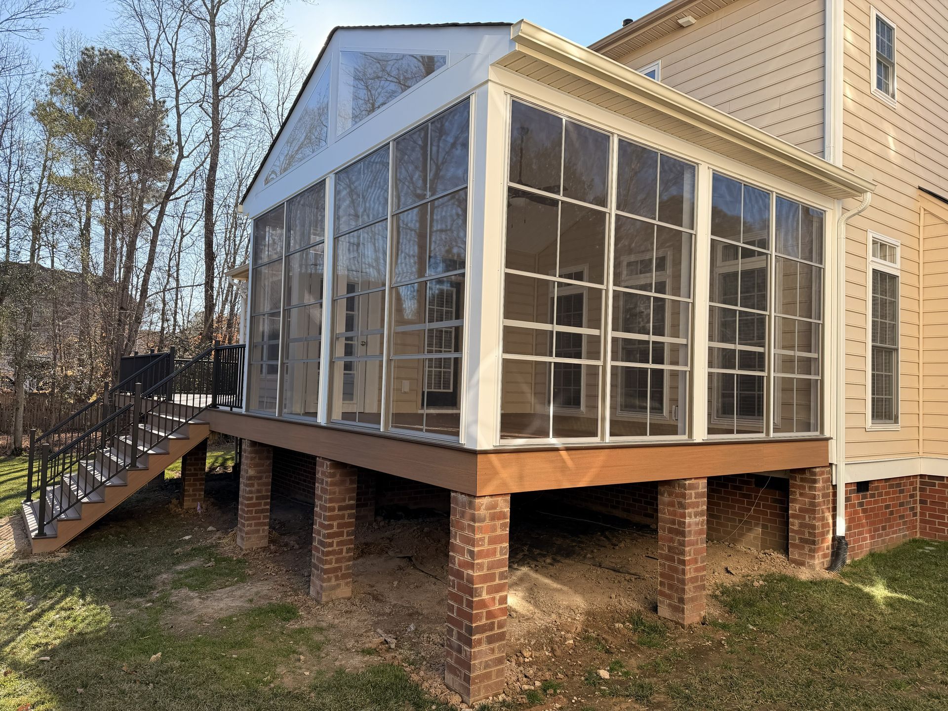 Enclosed porch with large windows and screened panels on a raised brick foundation beside a house.