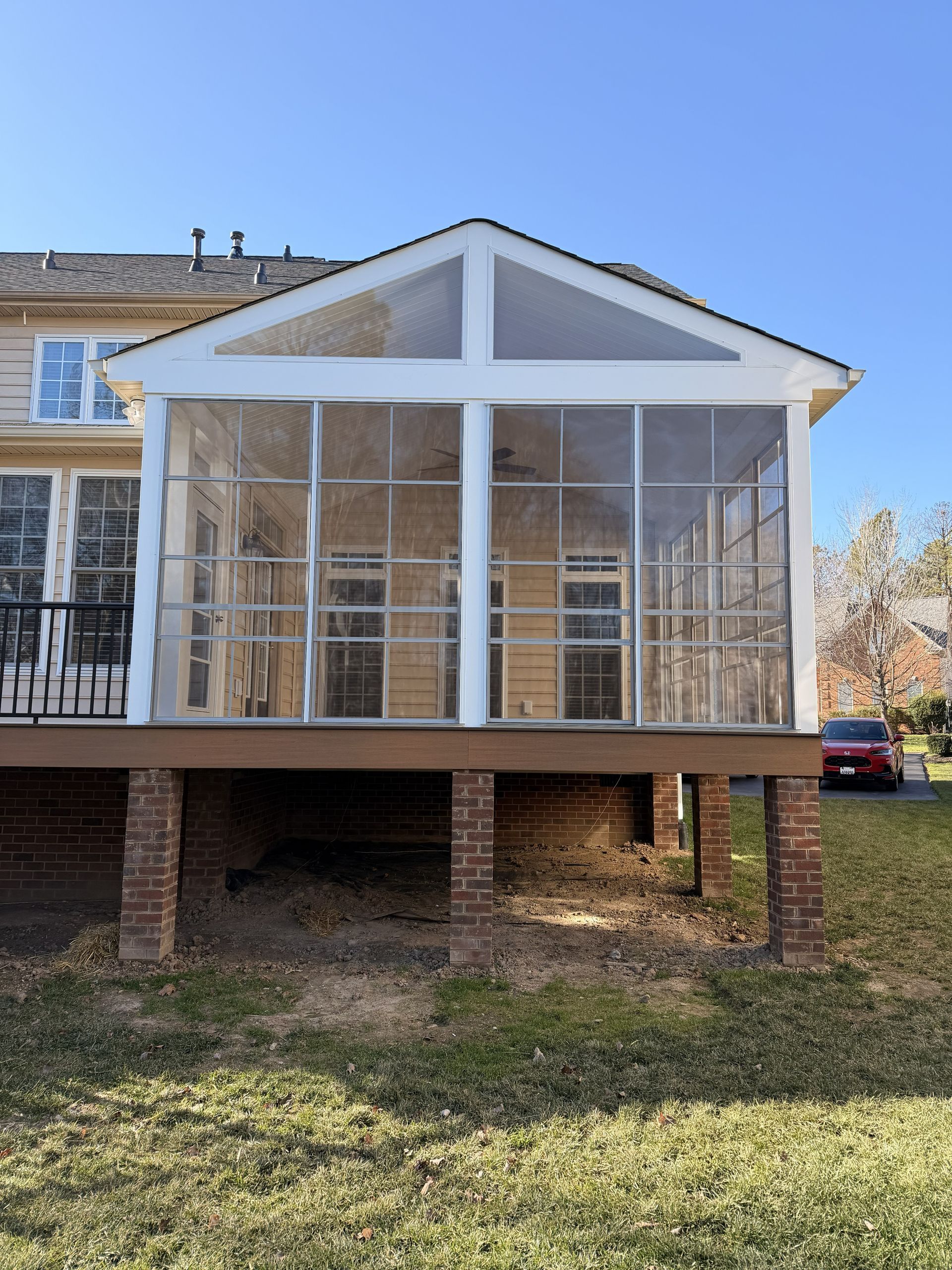 White screened porch with triangular gable on brick posts attached to a house.