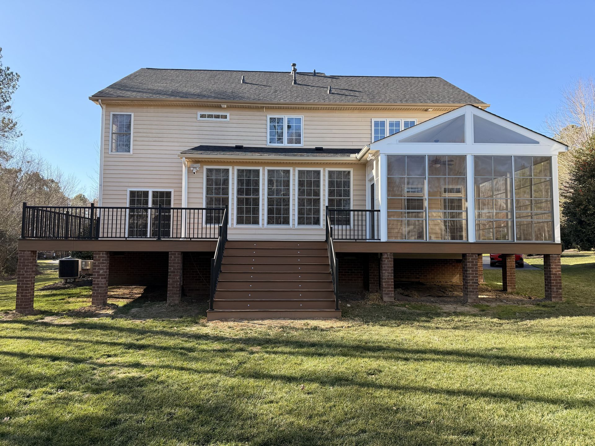 Rear view of a beige house with a raised wooden deck, stairs, and screened porch in a grassy yard