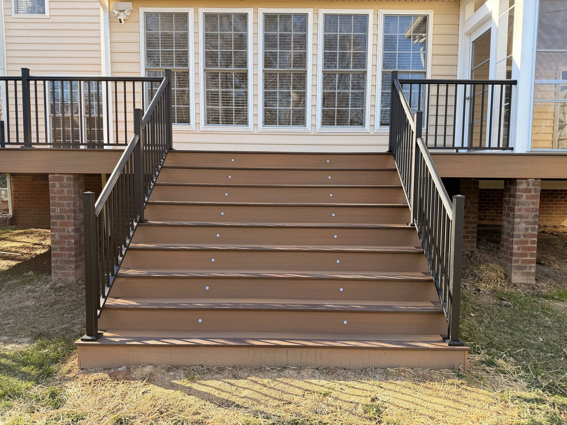 Brown front steps with black railings leading to a porch with glass doors and windows.