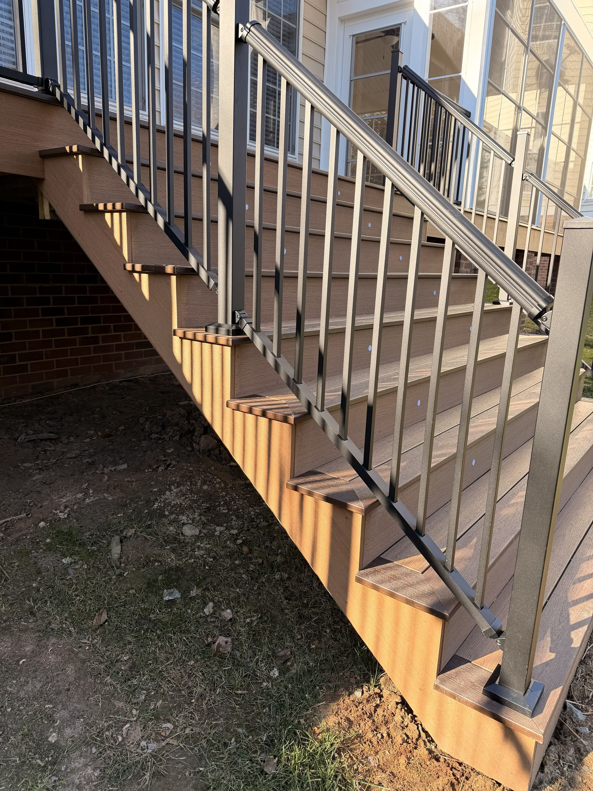 Outdoor wooden staircase with white railings beside a brick building, viewed from below.