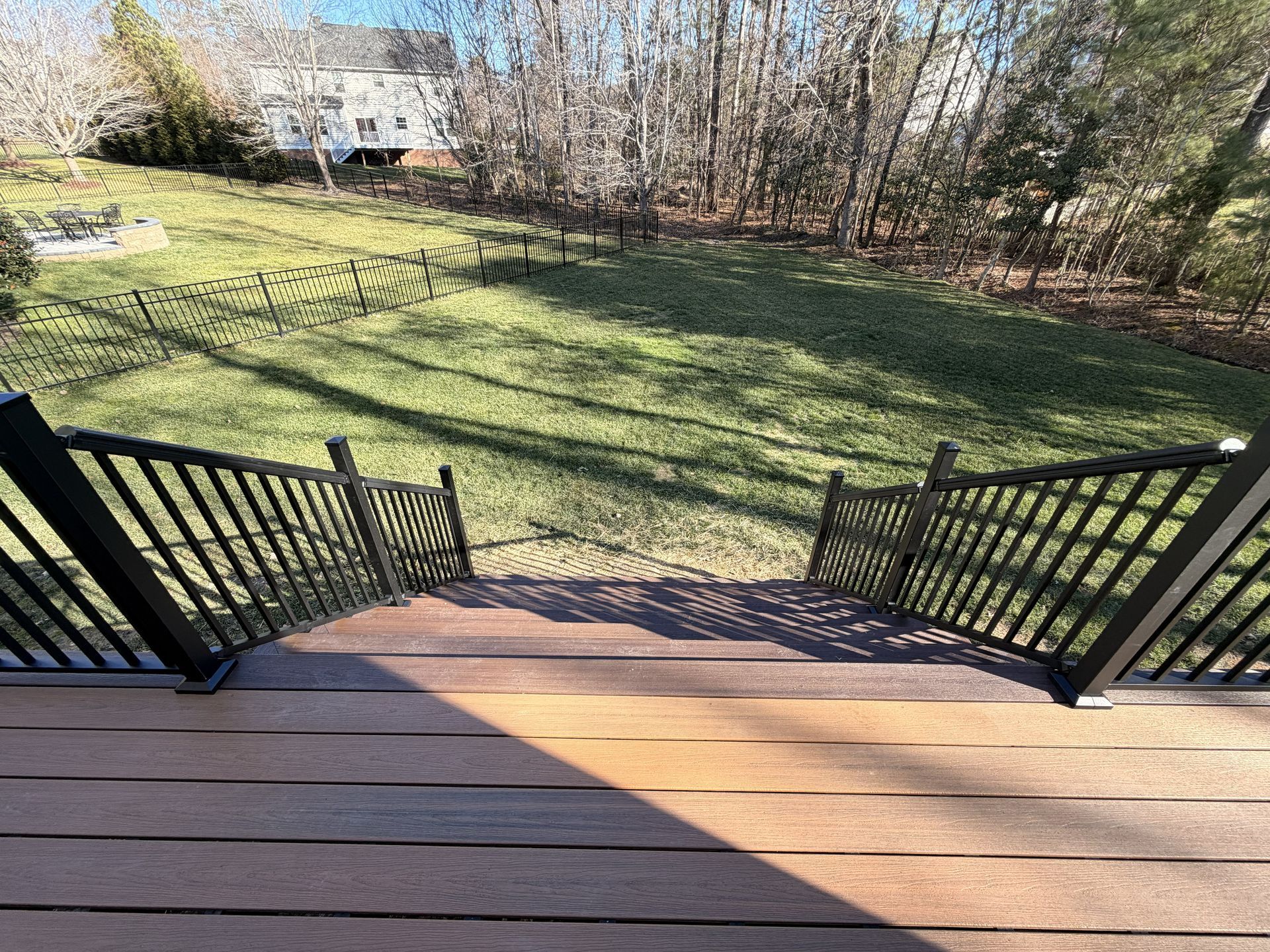 Back deck with black railings overlooking a sunny grassy yard and leafless trees