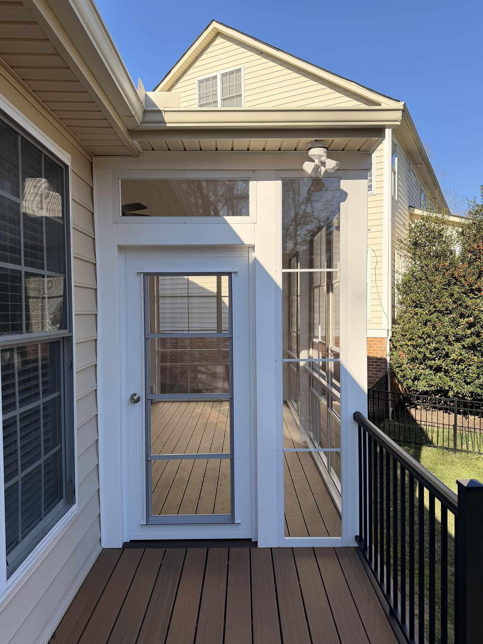 White front entry door with sidelights and a storm door on a narrow wooden porch, beside black railing.