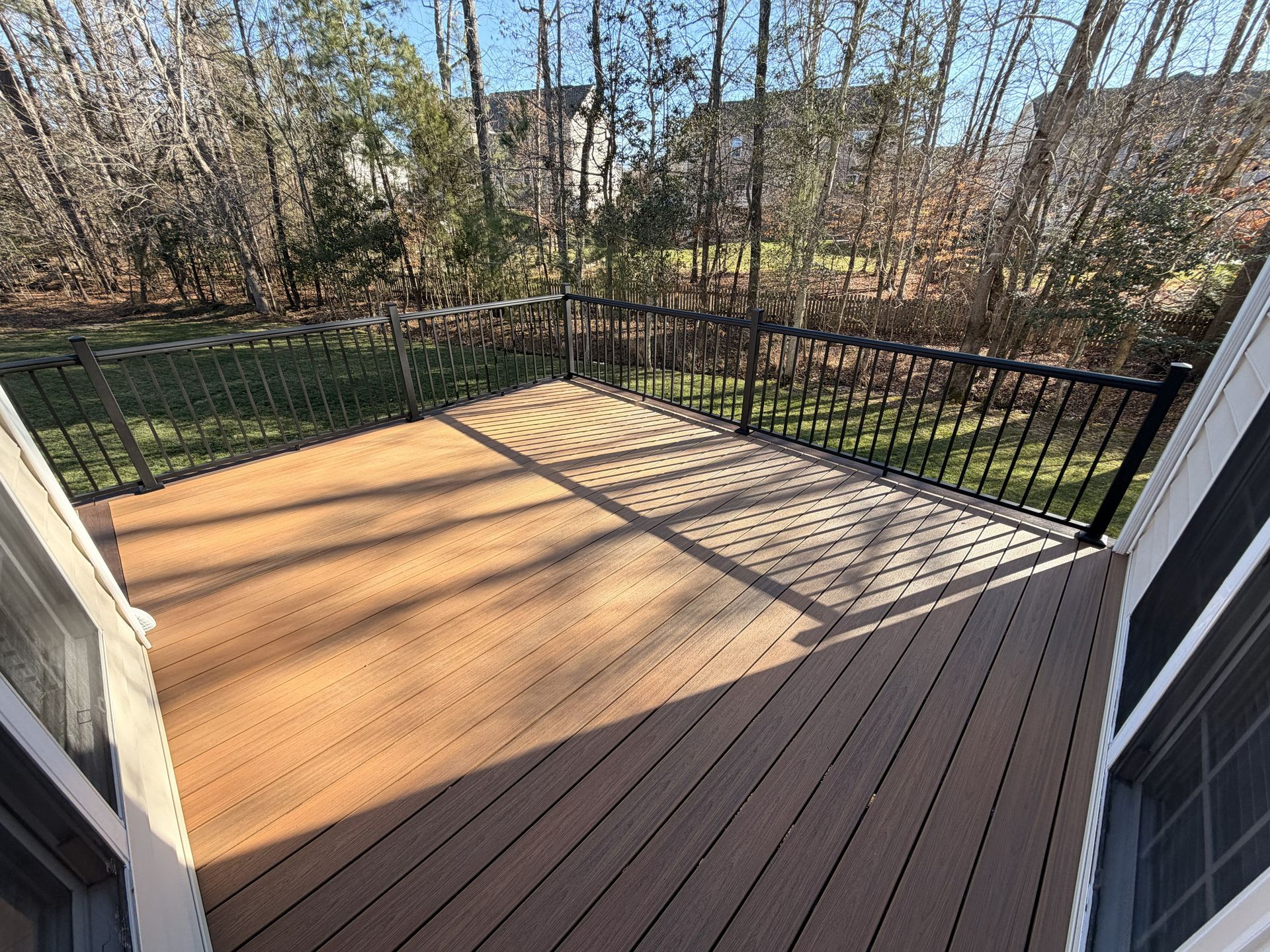 Small wooden deck with black railings, viewed from a doorway, with trees and yard beyond