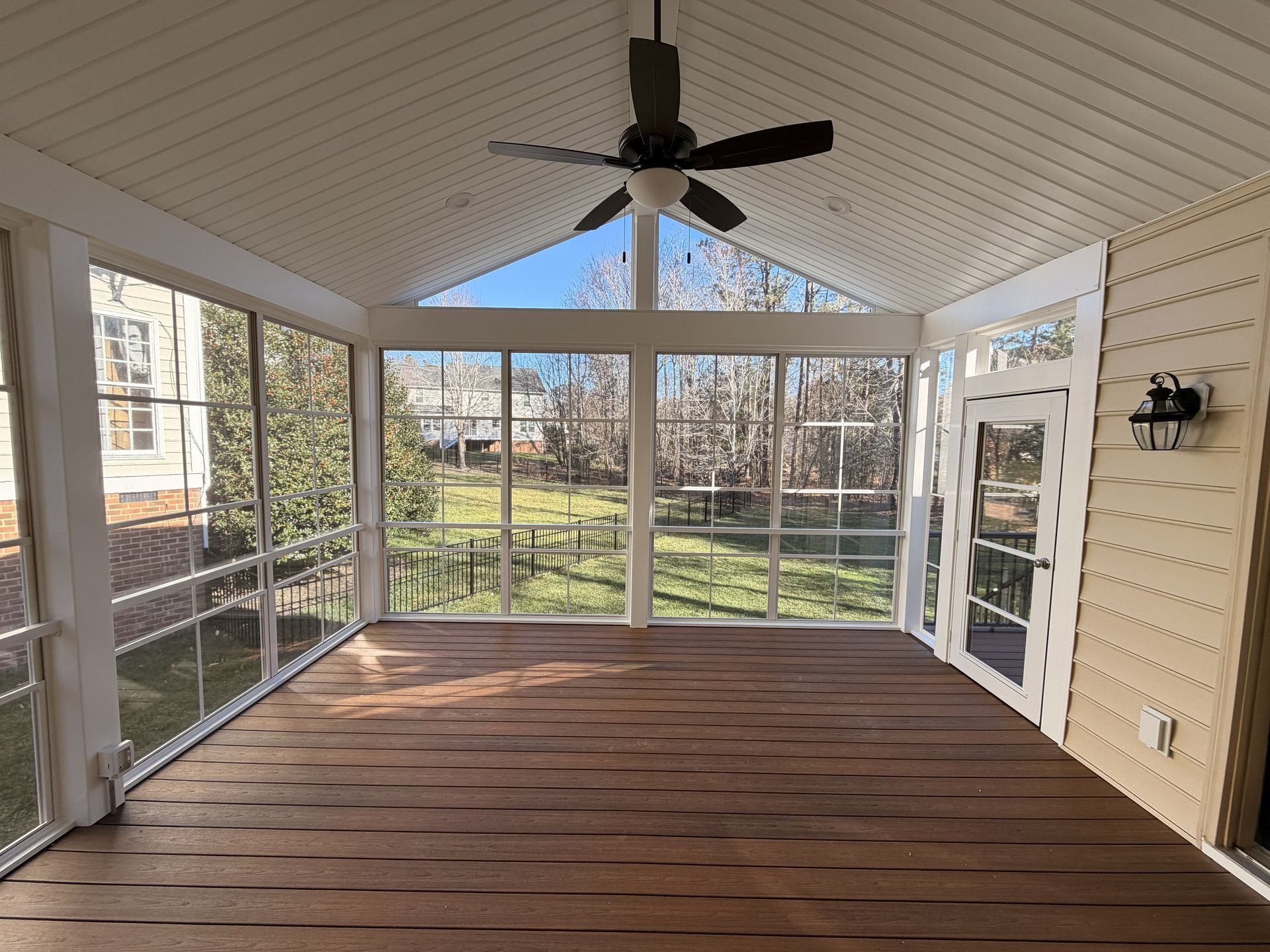 Empty screened porch with wood floor, white ceiling, ceiling fan, and large windows overlooking a yard