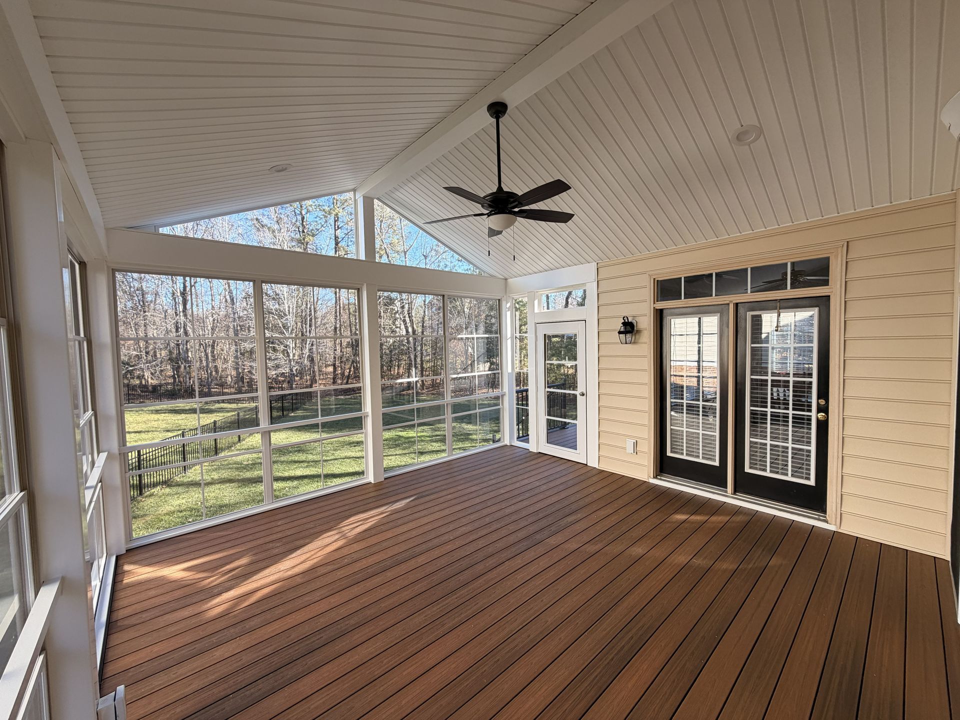 Covered screened porch with wood floor, white ceiling fan, and French doors overlooking trees