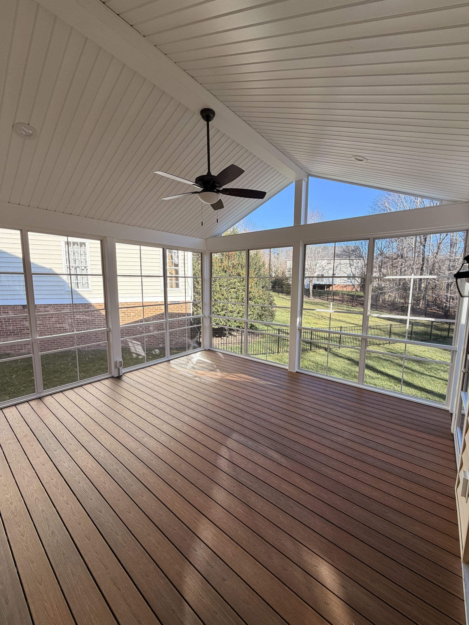 Covered porch with wooden floor, white ceiling and columns, ceiling fan, and a view of the yard.