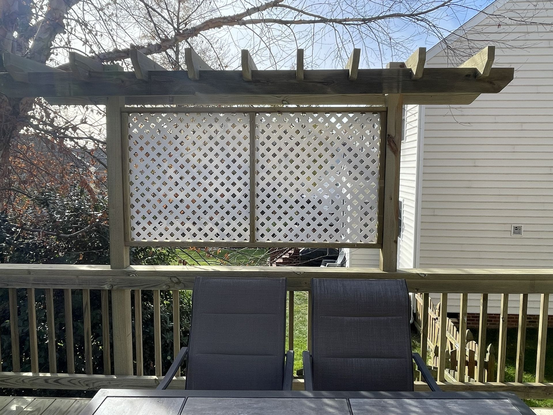 Backyard deck with two chairs facing a white lattice privacy screen and pergola.