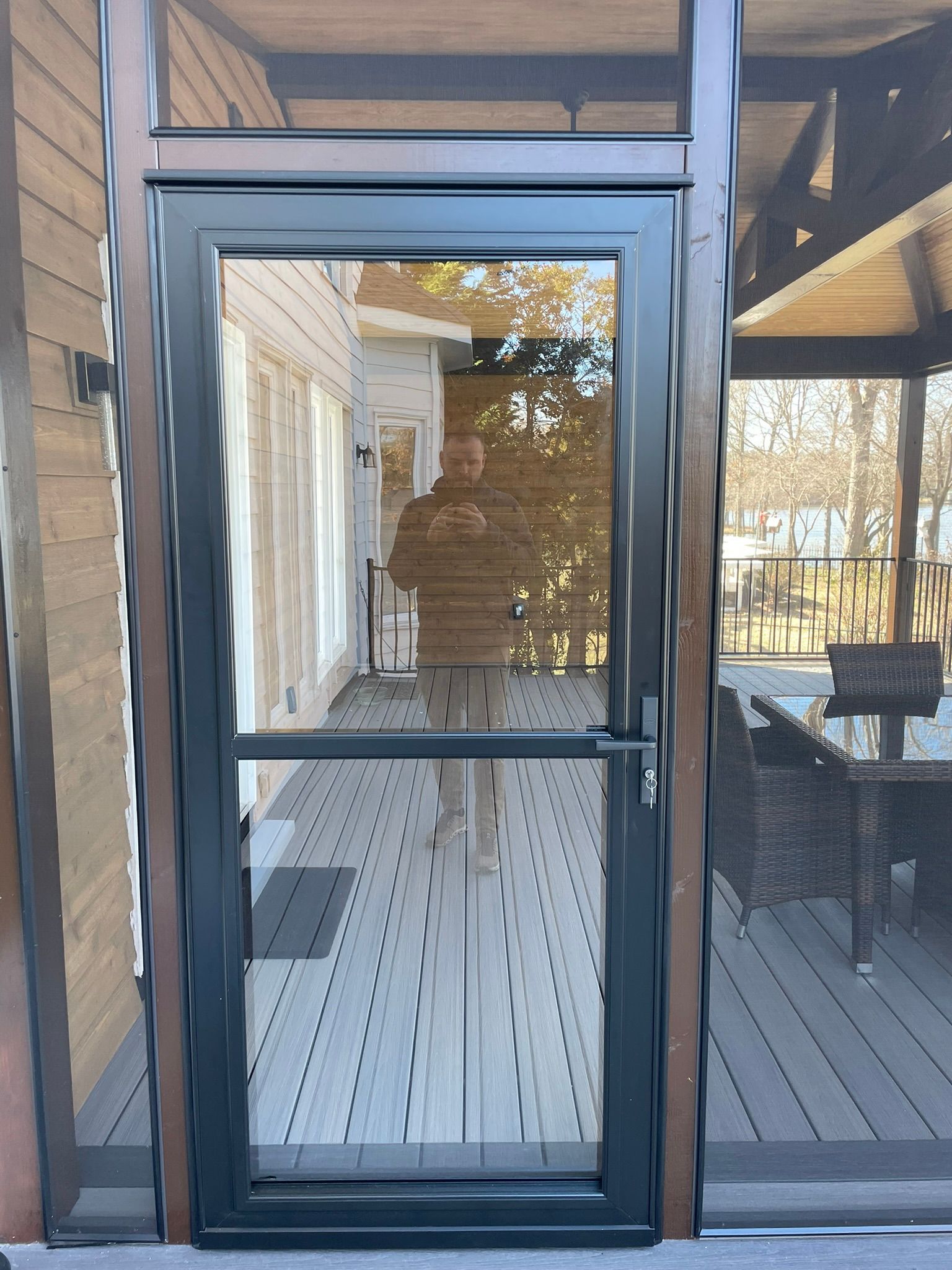 Black-framed glass screen door on a porch, reflecting a white house and outdoor seating area.