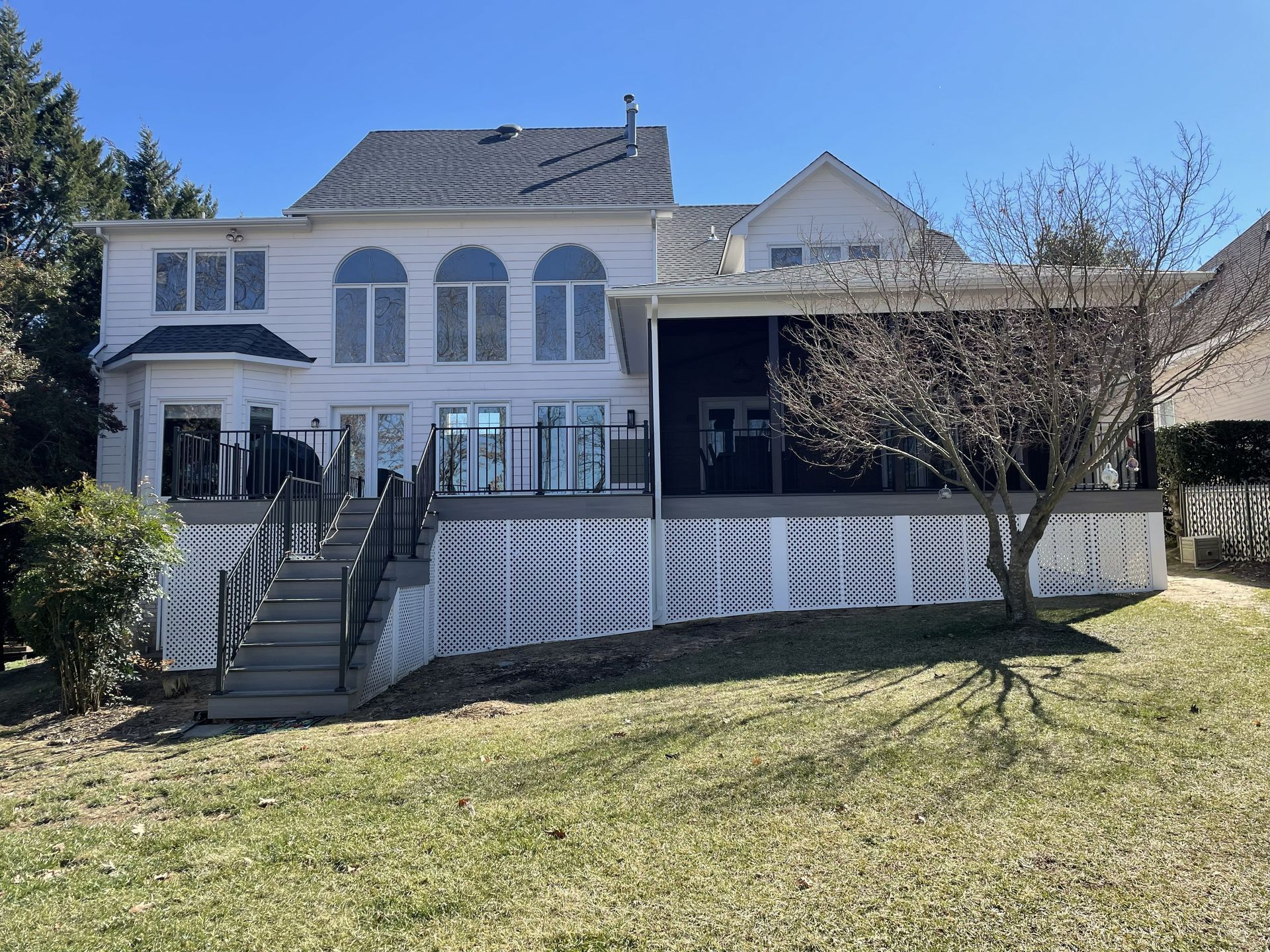 White two-story house with front stairs, porch, and black garage under a blue sky