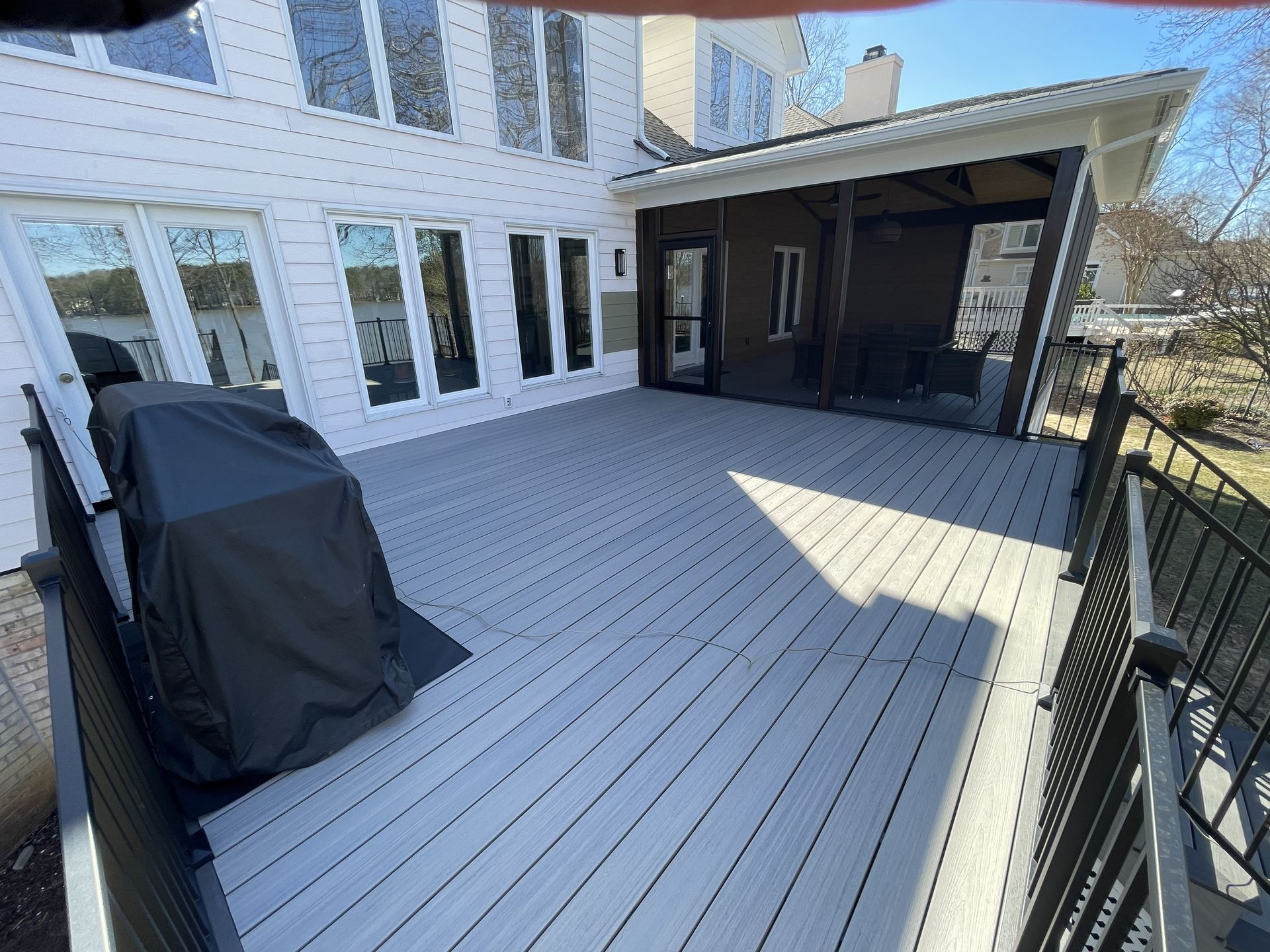Back patio deck with black grill cover and attached covered seating area beside a white house