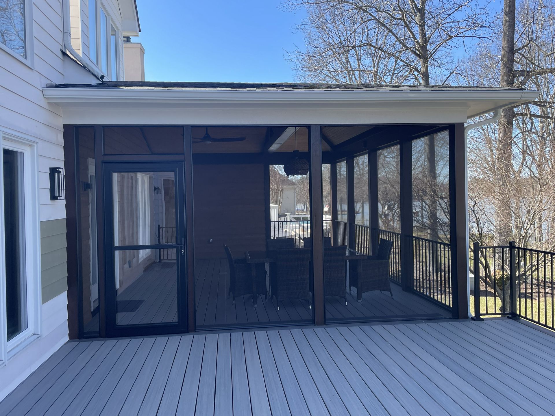 Screened porch with black framing and sliding doors attached to a house, opening onto a wooden deck.