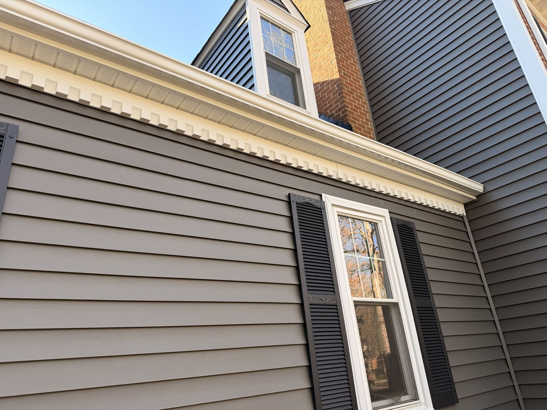 Exterior of a house with gray siding, white trim, black shutters, and a dormer window under the roofline