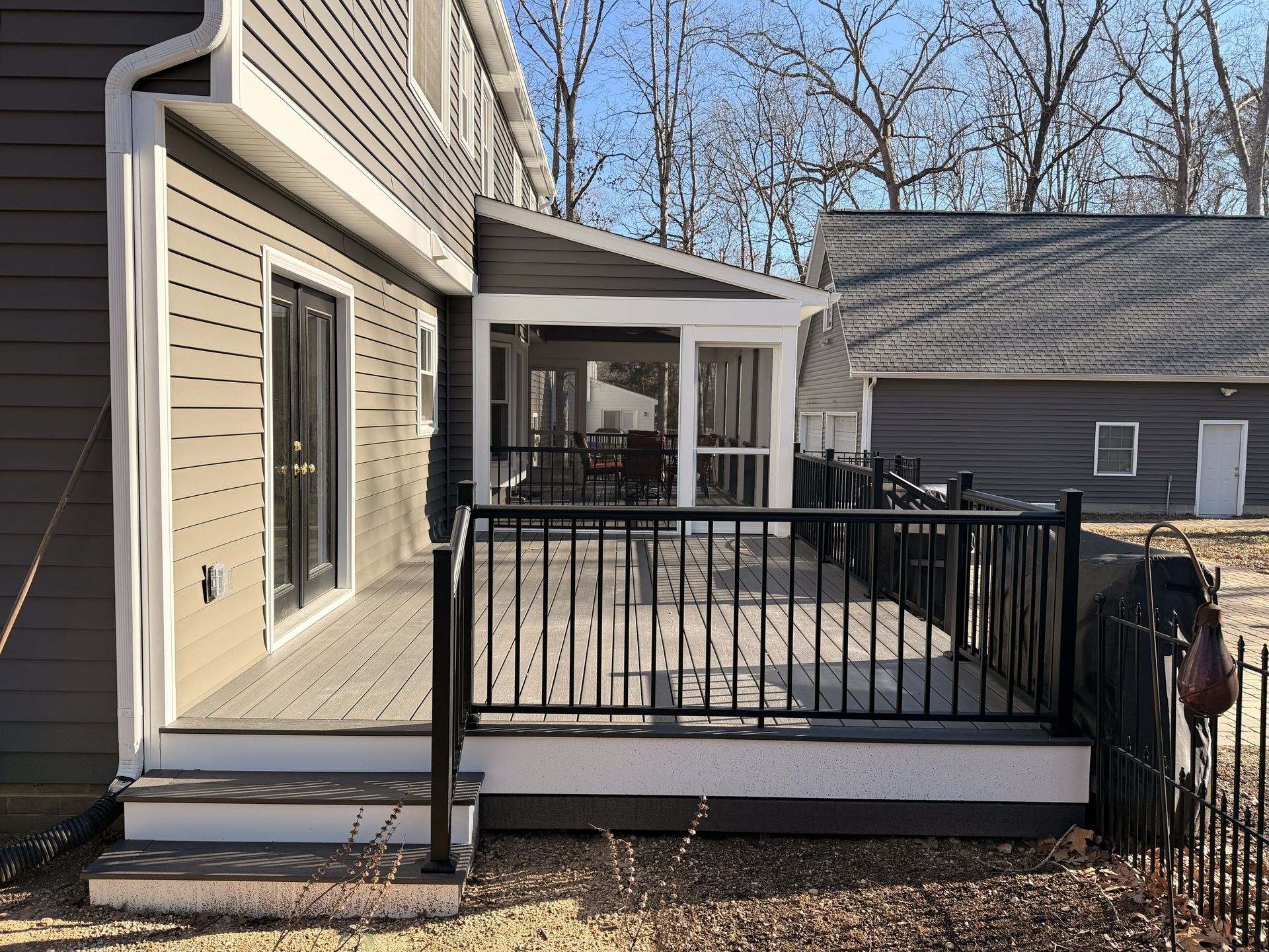 Backyard deck with black railing, beige siding, and a patio leading to a gray garage.