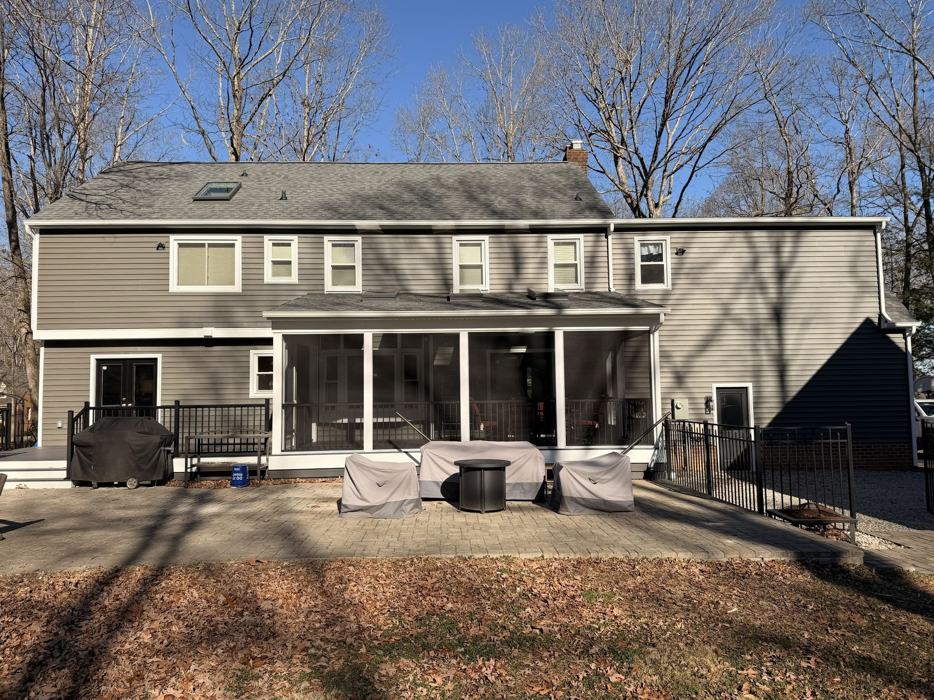Two-story gray house with a patio, sliding doors, and a fenced yard in winter.