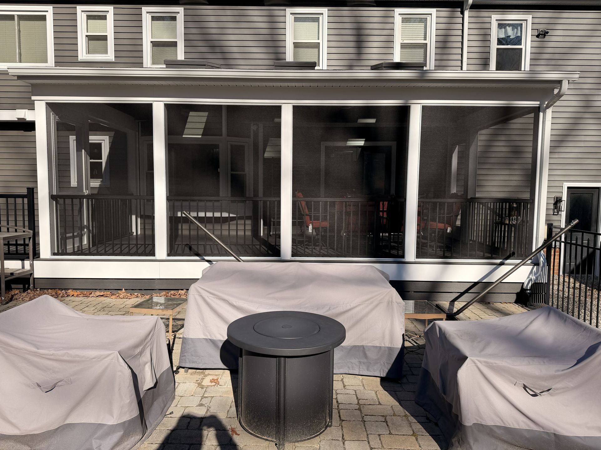 Covered patio with screened porch, black table, and two covered grills in front of a gray house