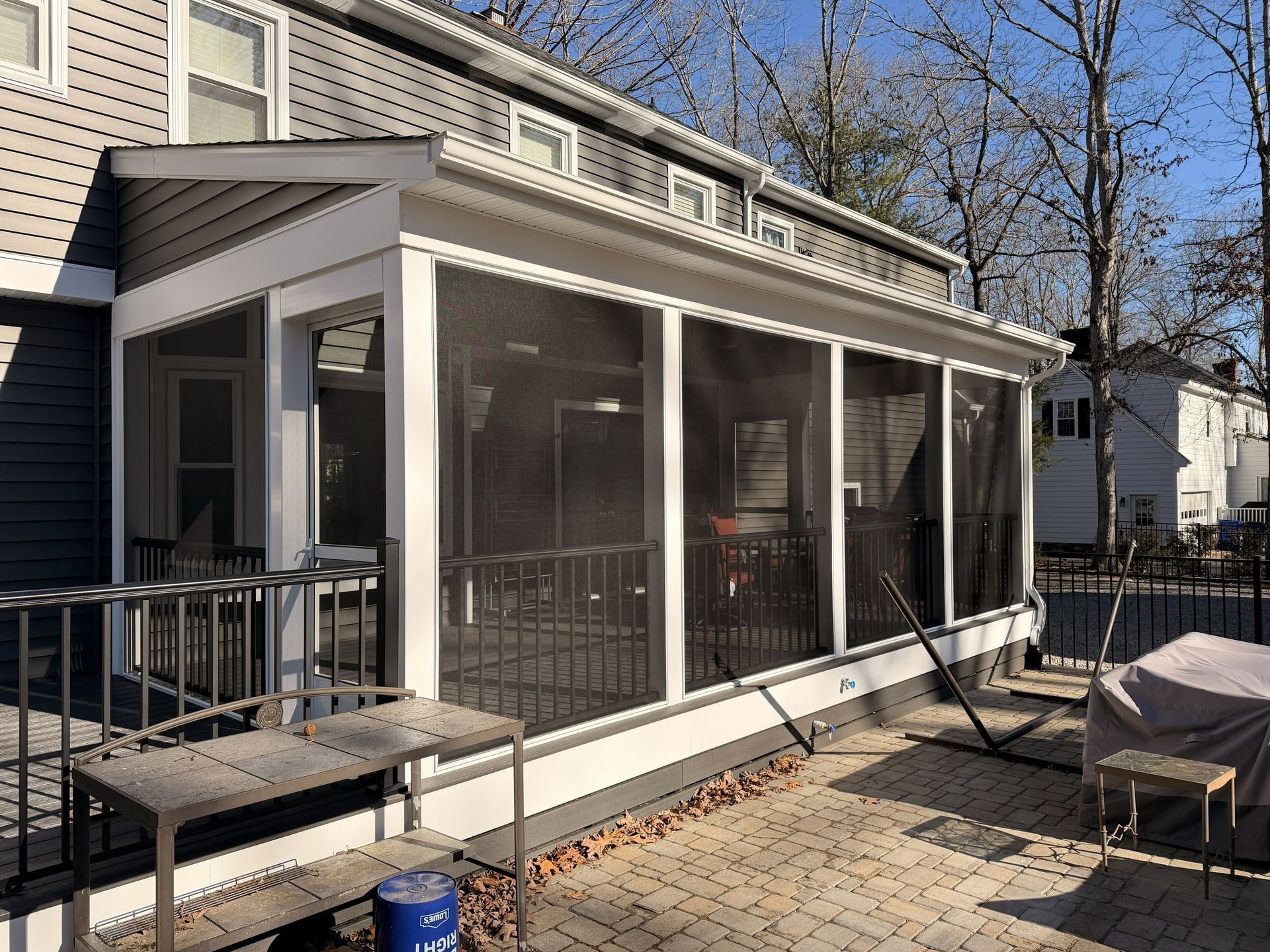 Screened-in porch on a house with patio furniture and a paved backyard area