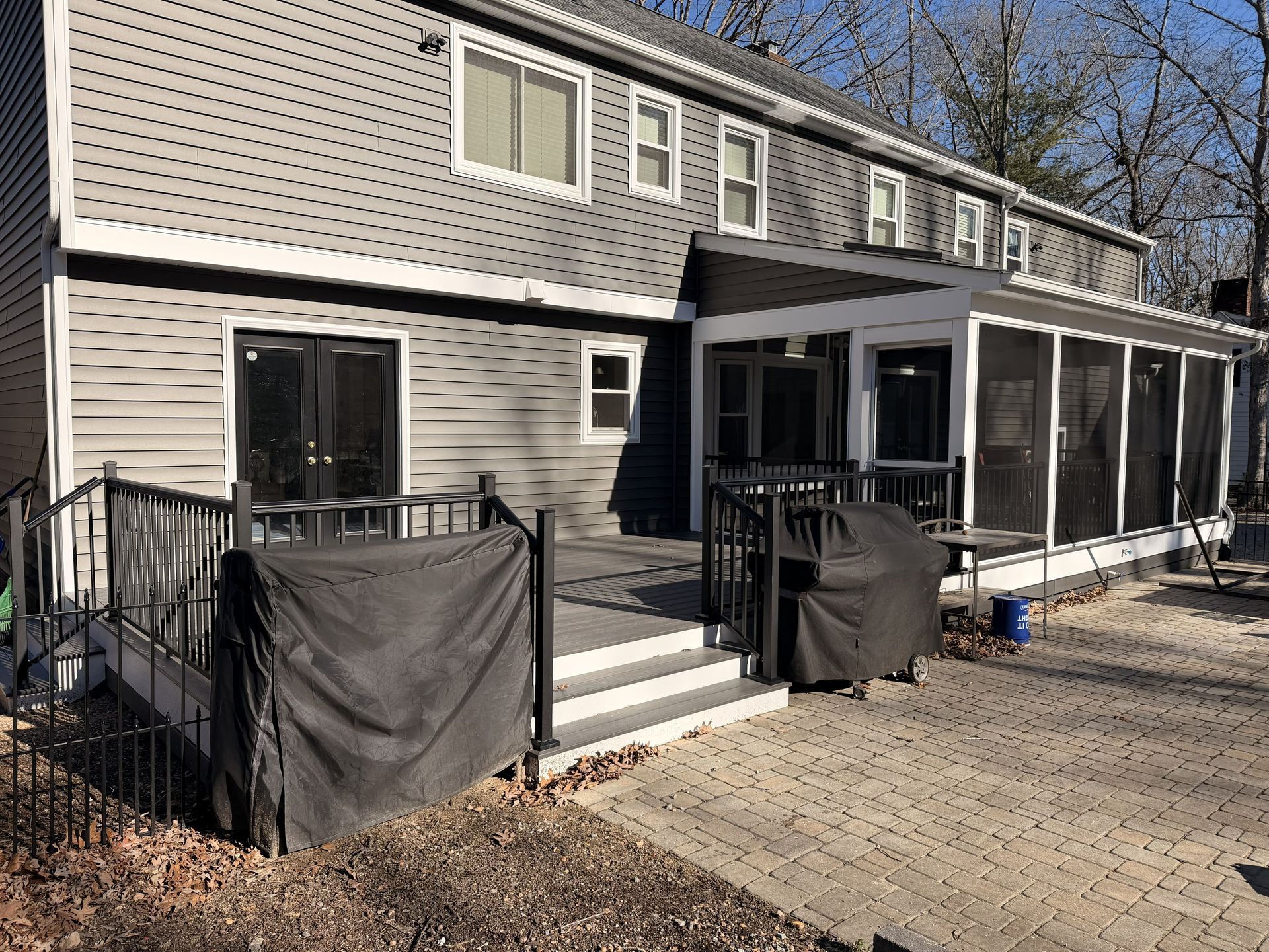 Two-story beige house with a screened porch, black railings, and steps leading to a gravel driveway