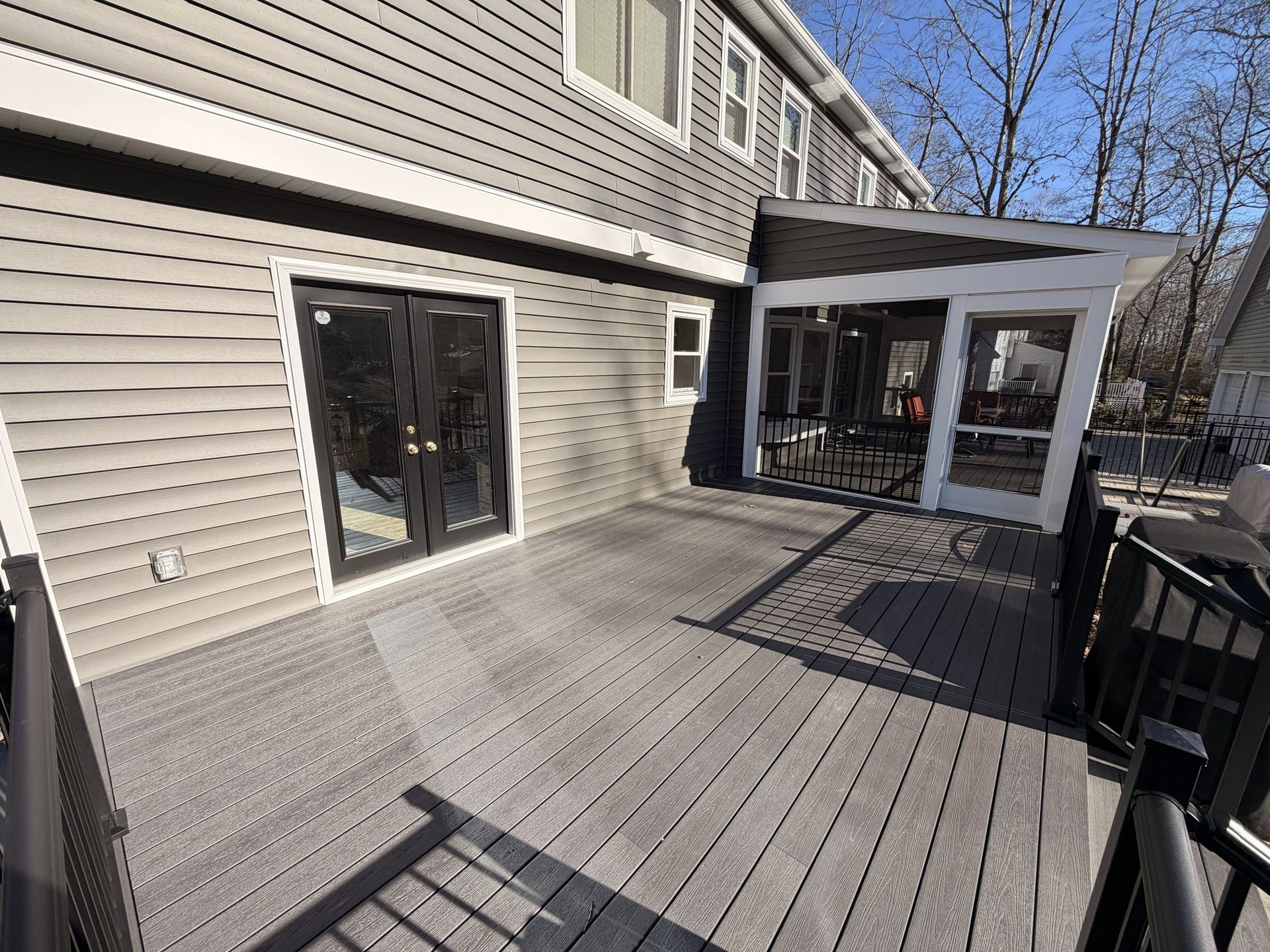 Gray deck beside beige house with sliding glass doors and a screened porch under a clear sky