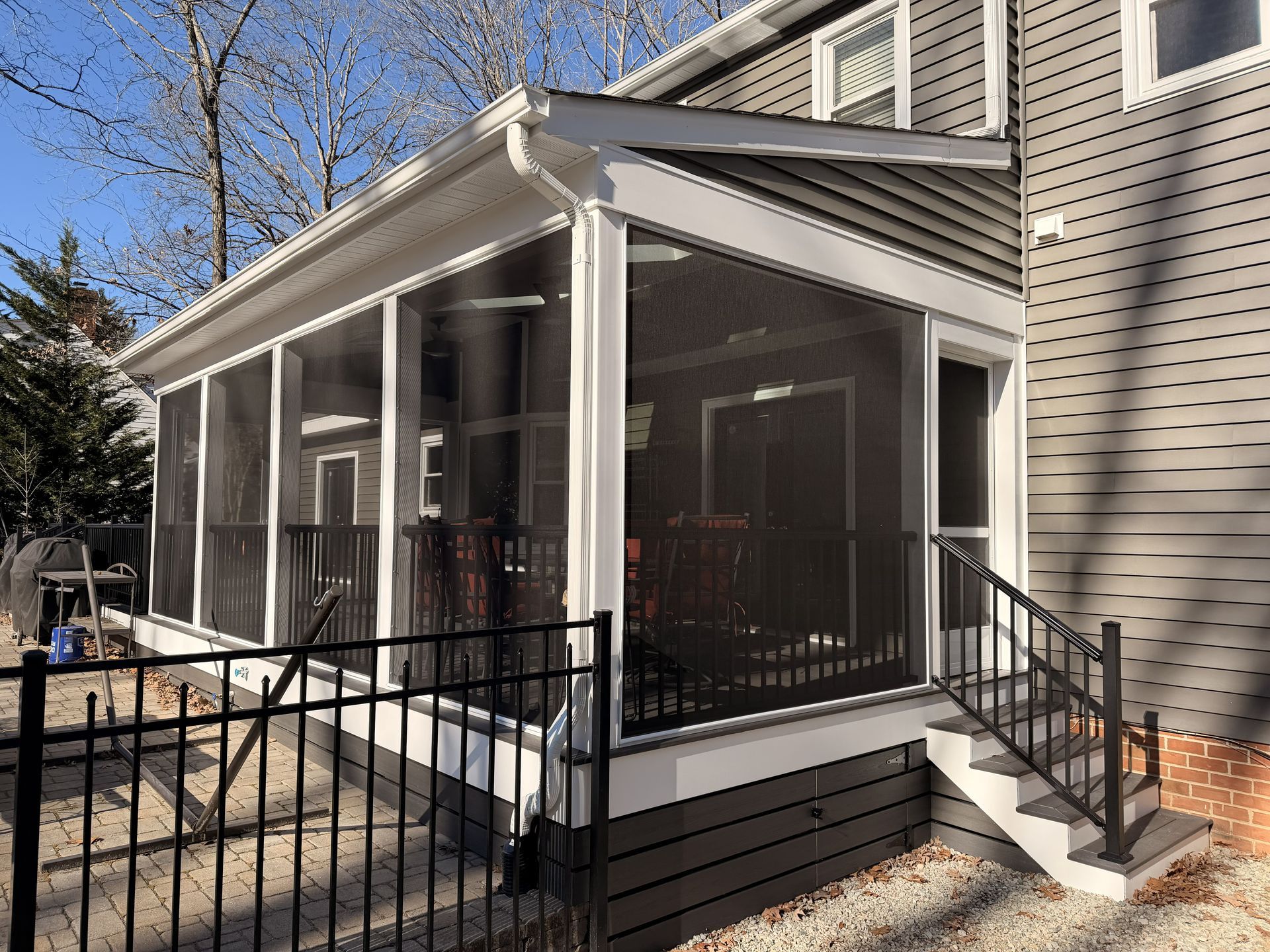 Screened porch with white trim and black railing attached to a house on a sunny day