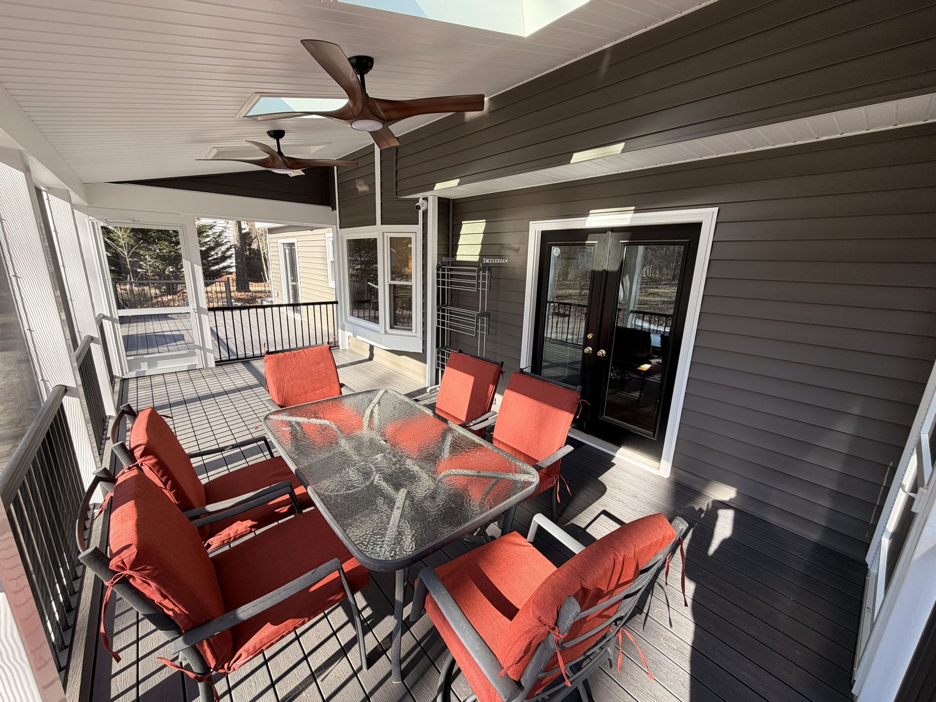 Covered patio with red chairs around a glass table and ceiling fan, beside a screened porch door.