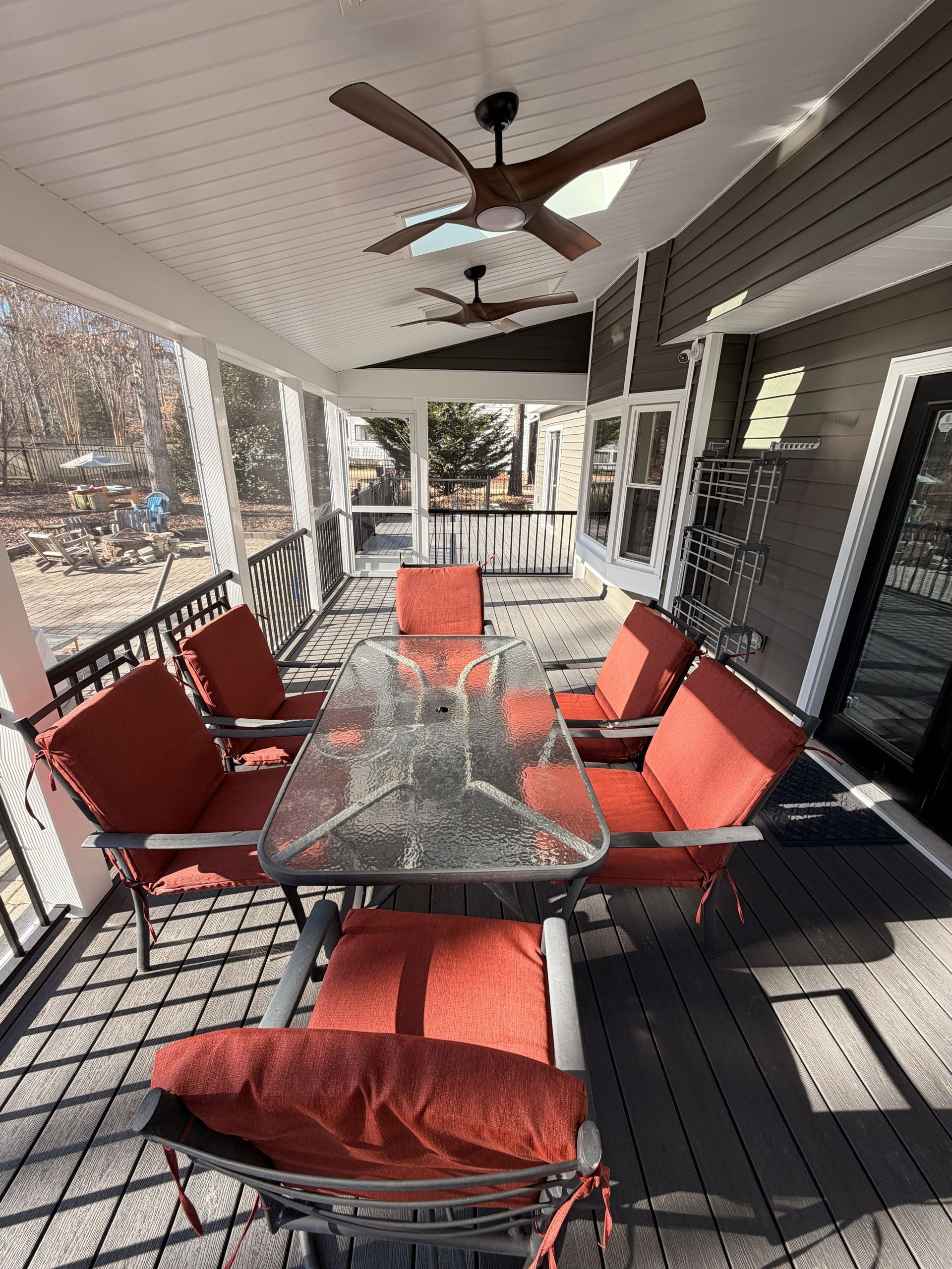 Covered porch with glass-top table, orange-cushioned chairs, and ceiling fans.
