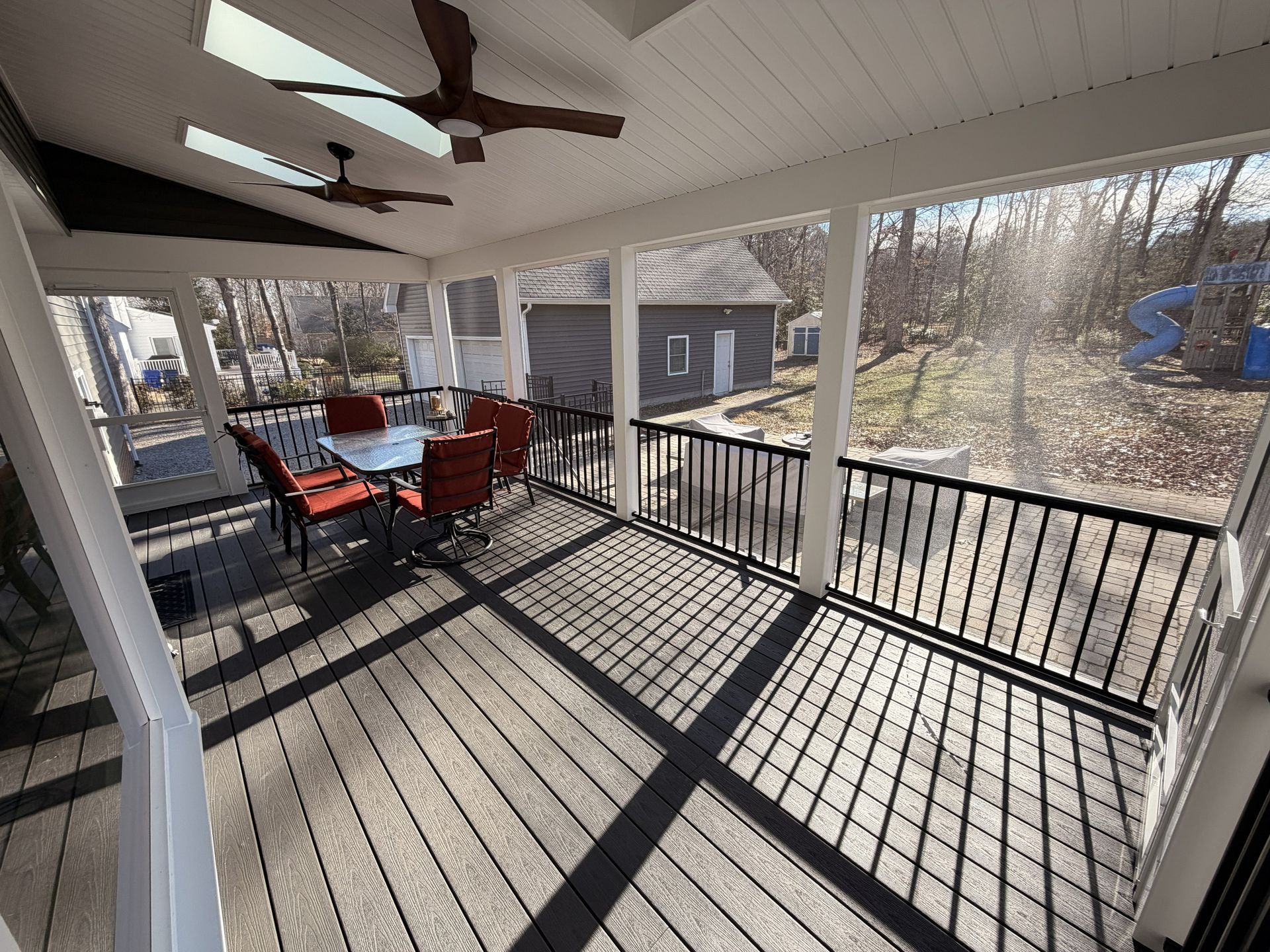 Covered porch with red chairs, black railing, and long shadows in winter sunlight.