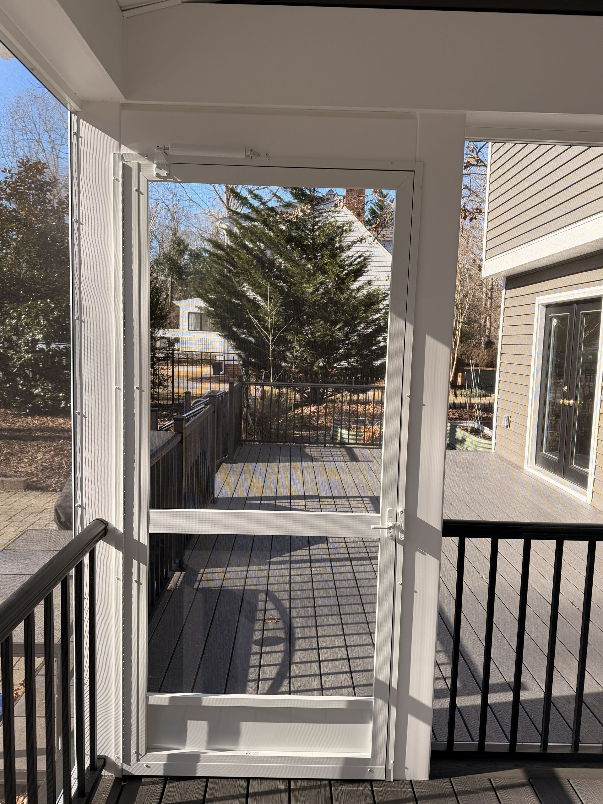 Front porch with white columns, black railings, and a paved walkway leading to a backyard gate.