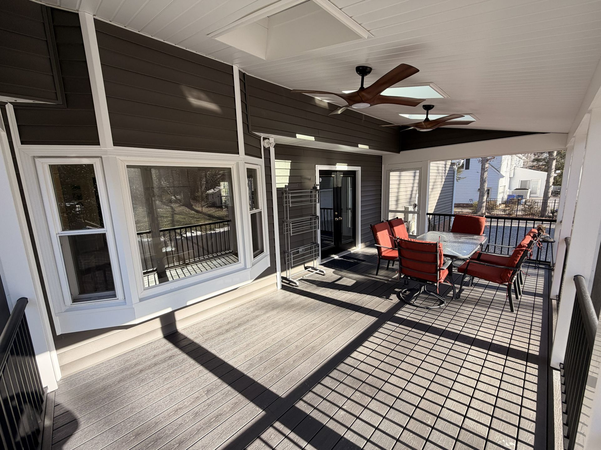 Covered patio with red chairs and table, sunlight casting shadows across the deck.