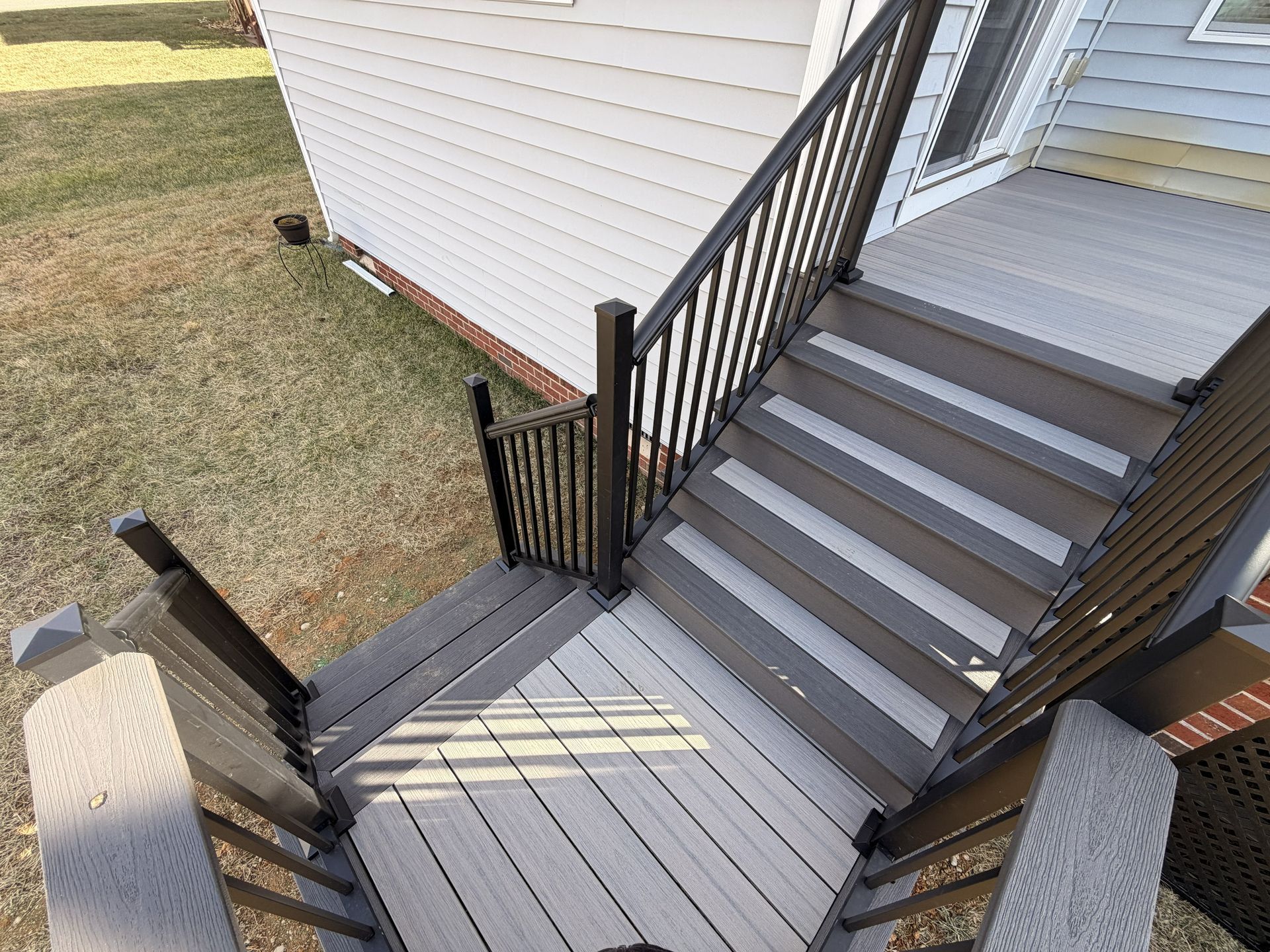 Exterior wooden staircase and landing with dark railings leading to a white-sided house entrance.