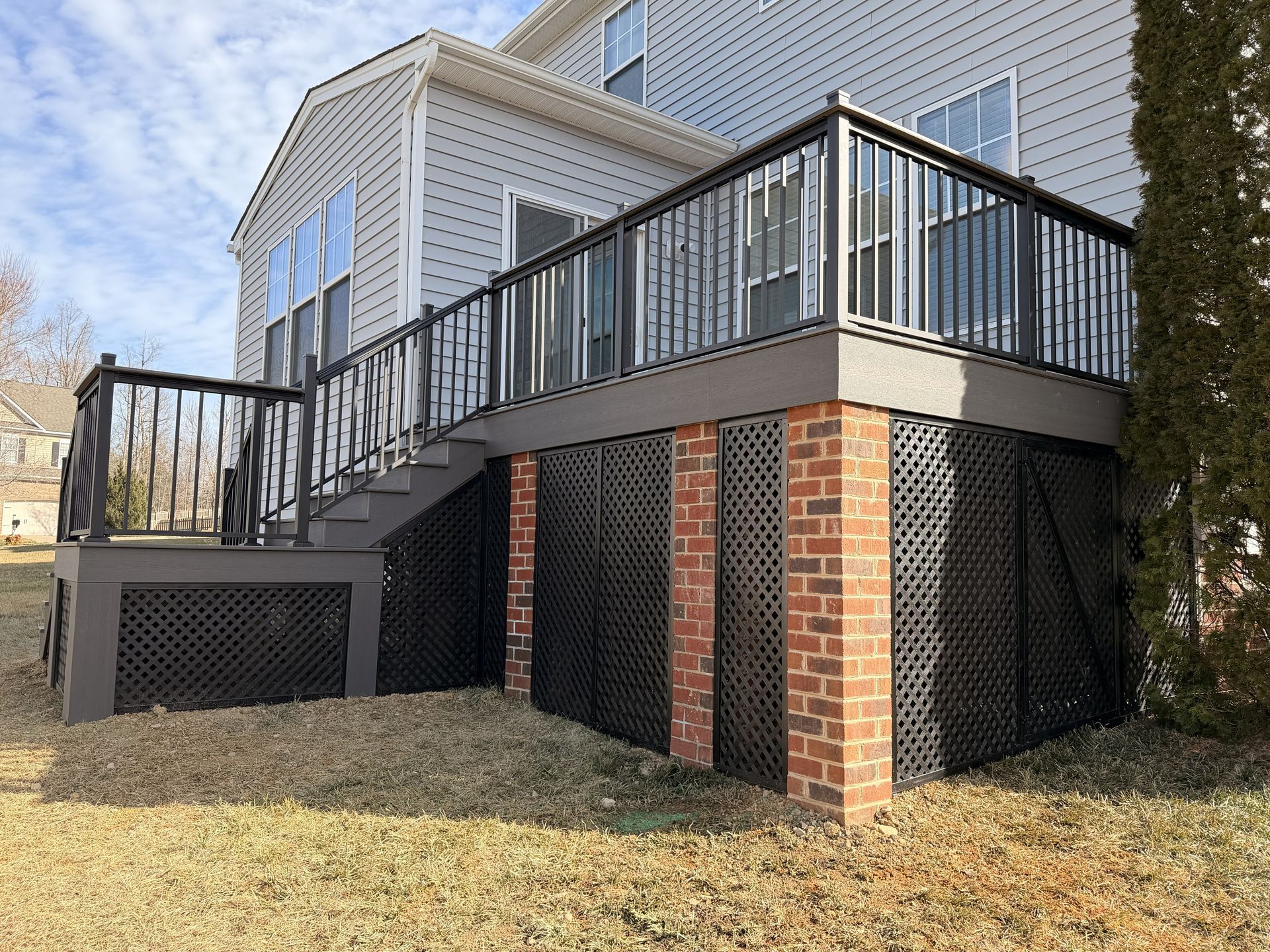 Raised house deck with black railings, brick columns, and lattice skirting on a grassy slope