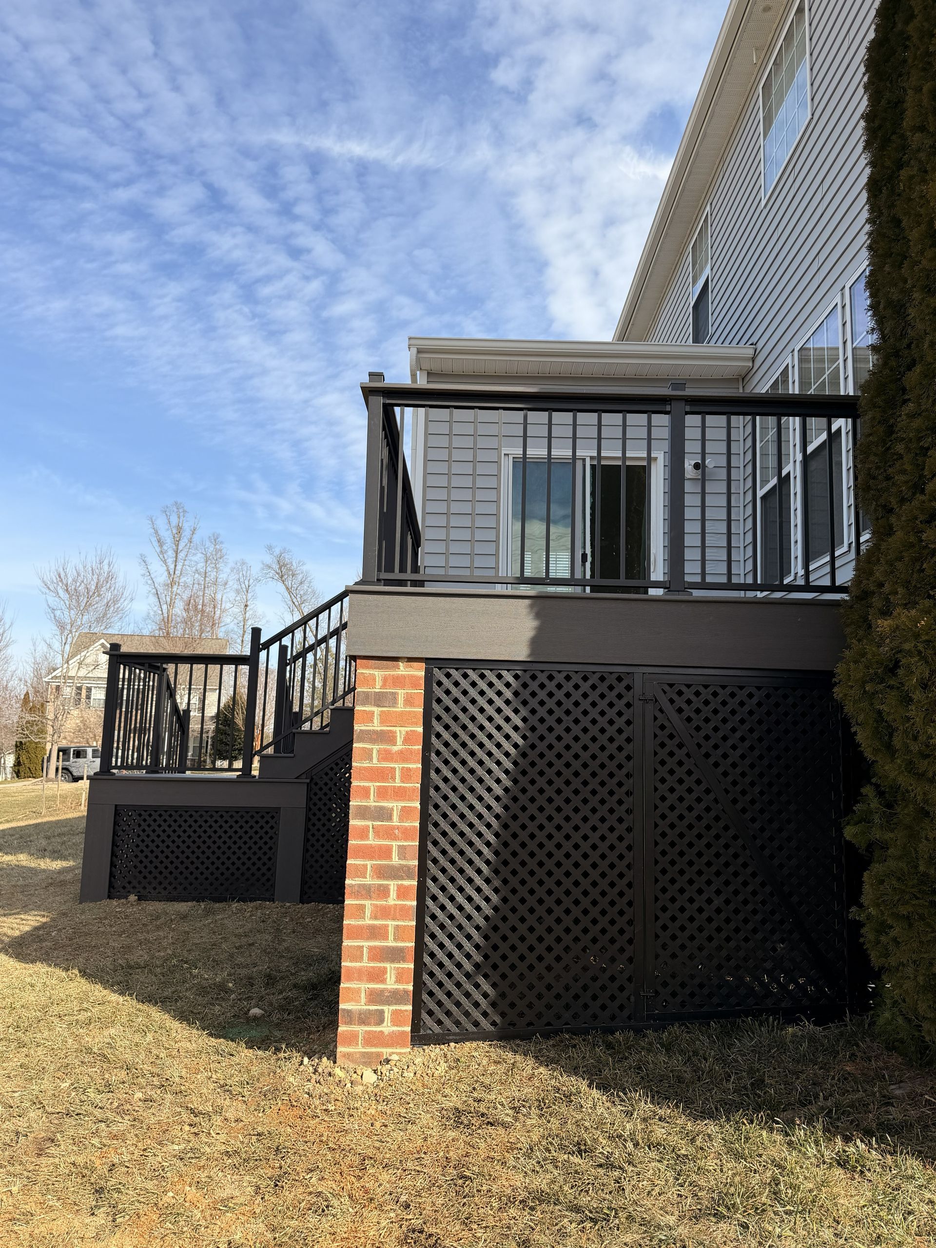 Back deck with black railings and brick posts beside a house, under a blue cloudy sky