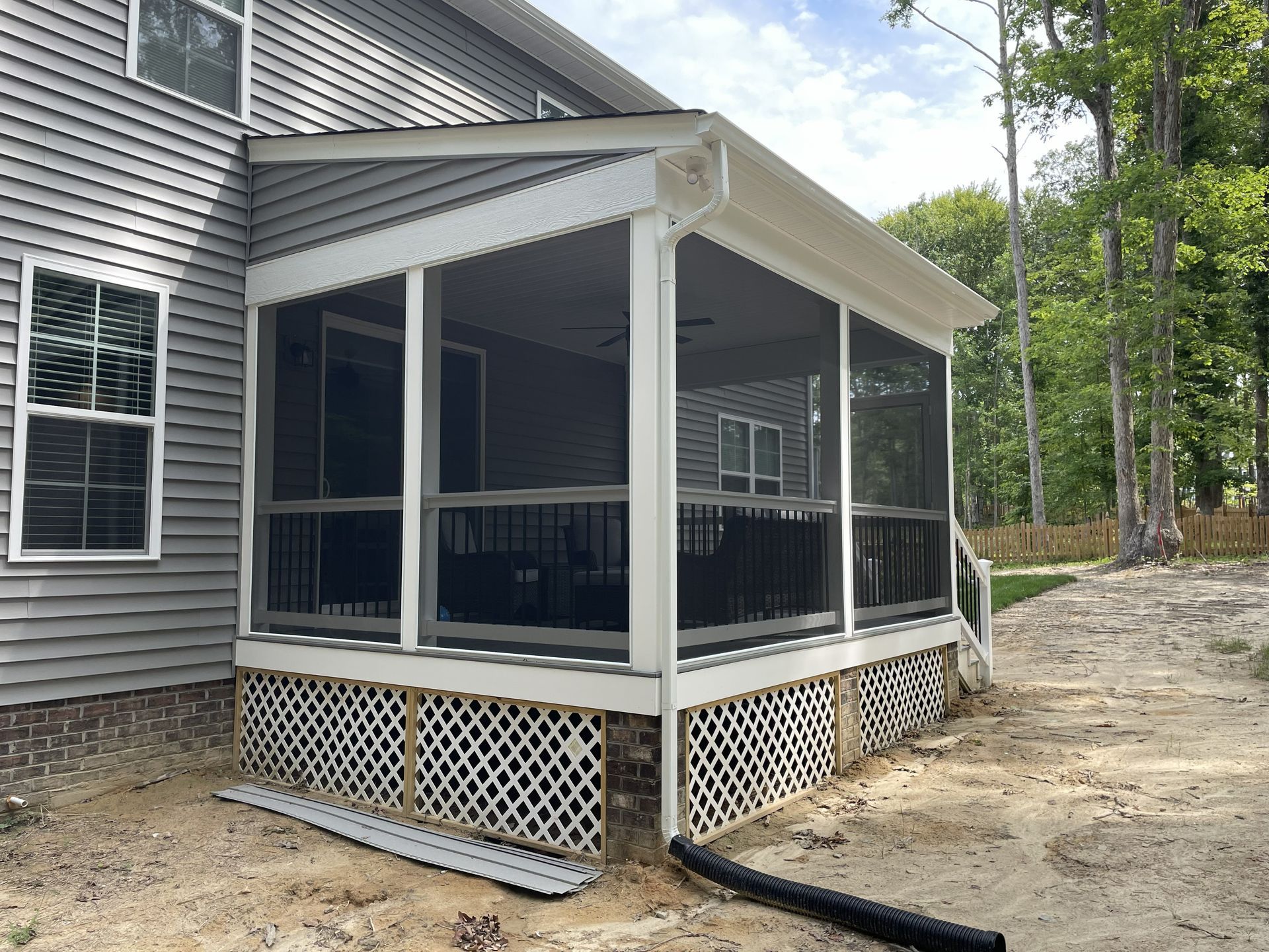 Screened porch addition on a gray house with white trim and lattice skirting, beside a wooded yard