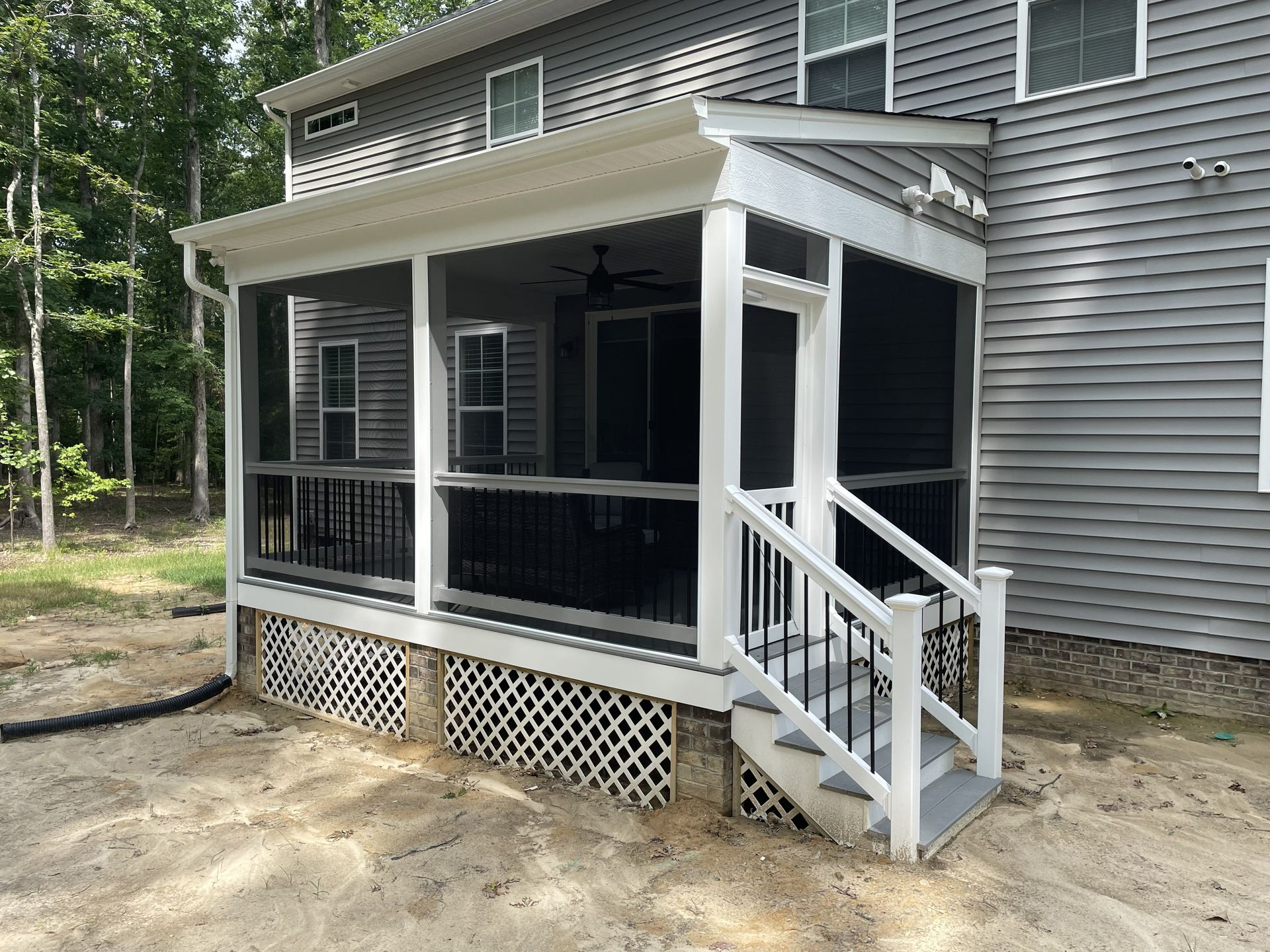 Small screened porch with white stairs and black railing on a gray house in a wooded yard