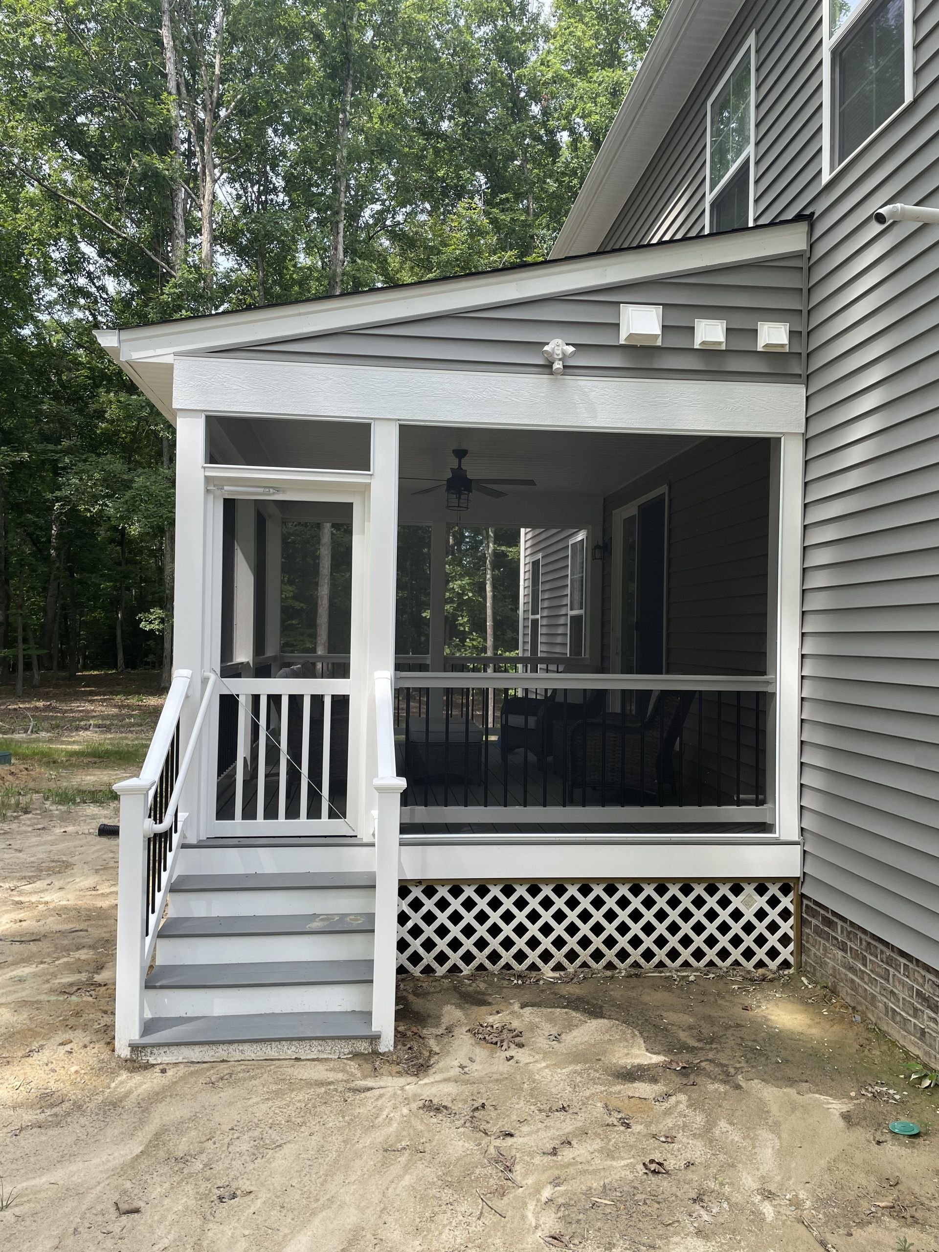 Small covered porch with white railings, steps, and lattice skirting beside a gray house.