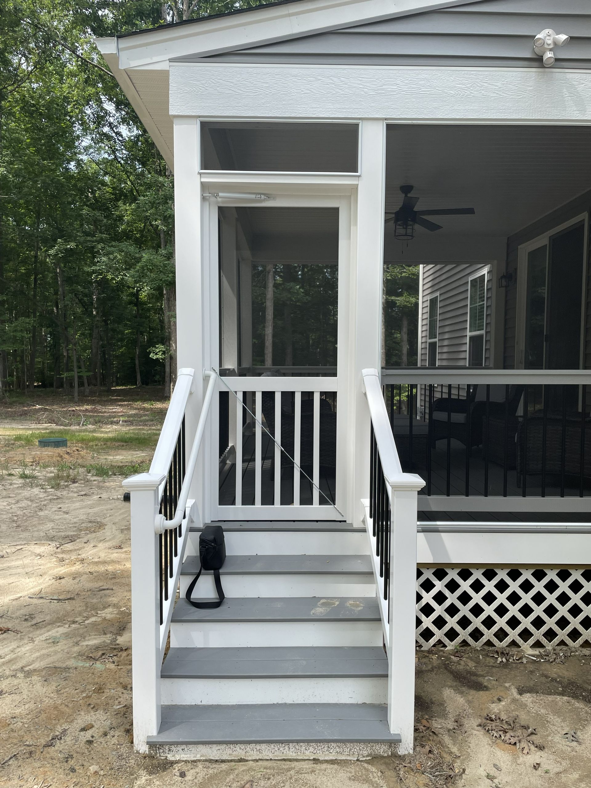 Front porch steps with white railings leading to a screened entry on a gray house