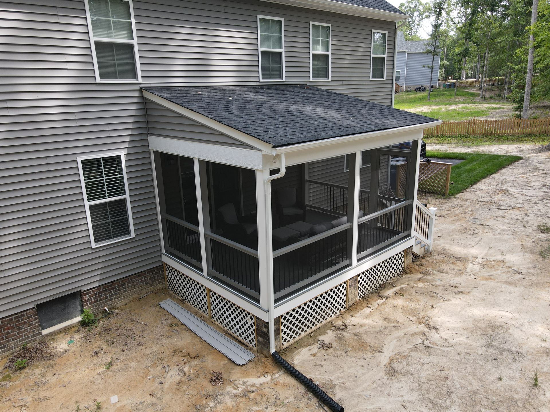 Screened porch addition on a gray two-story house, with white trim and gravel yard nearby