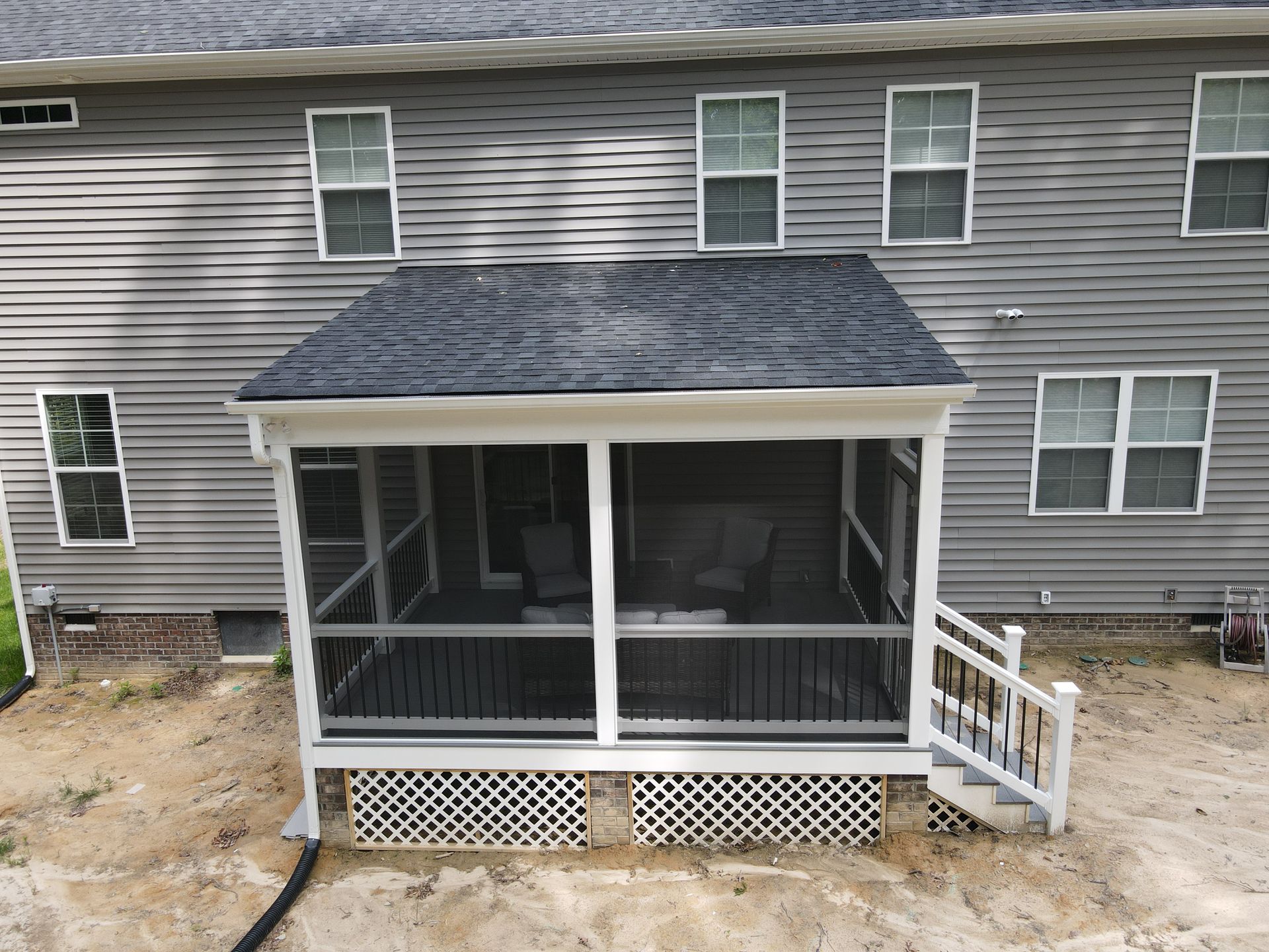 Covered back porch with screened walls and white railing on a gray two-story house.