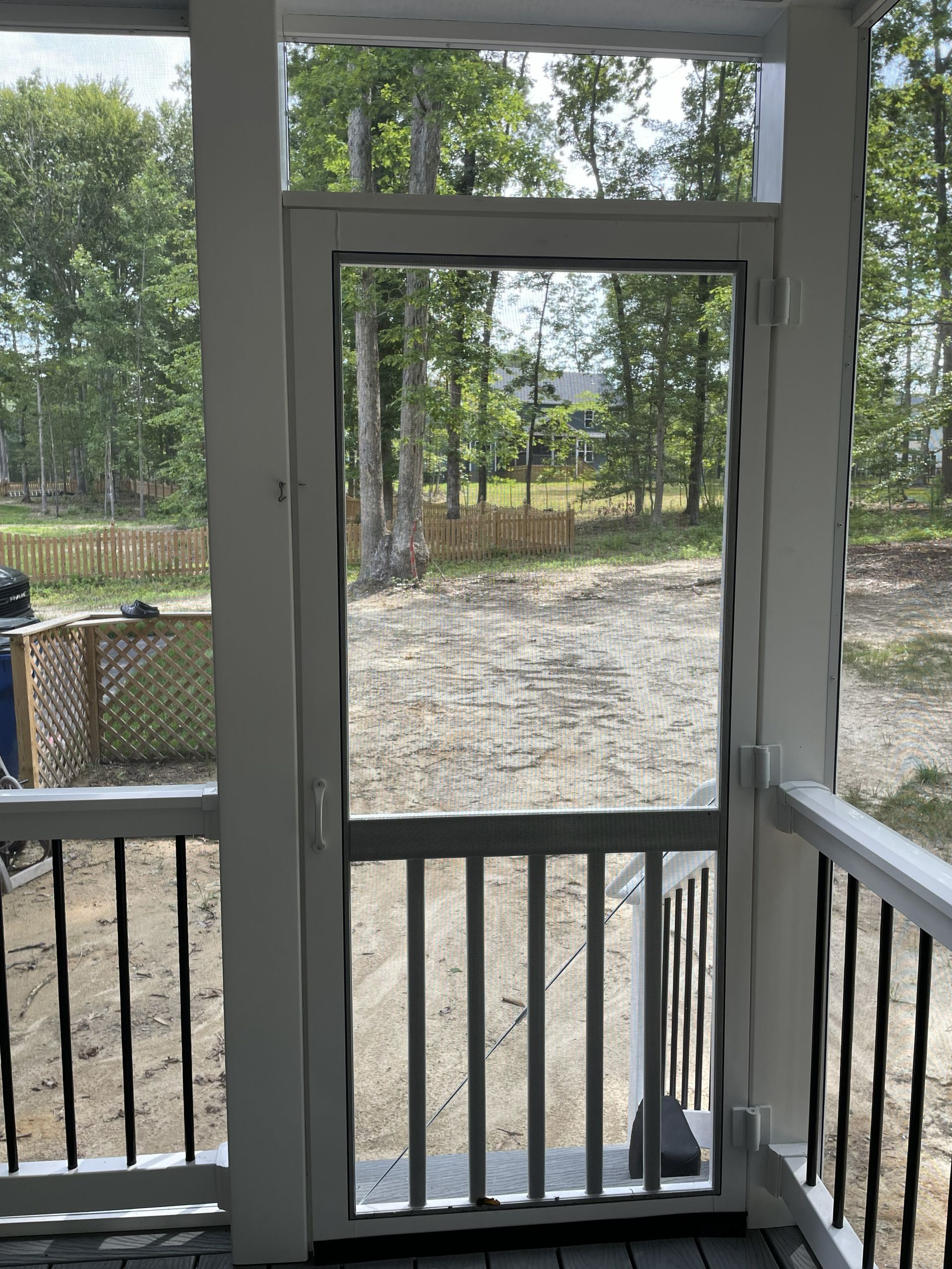 View from a porch doorway to a gravel yard and trees beyond a black railing