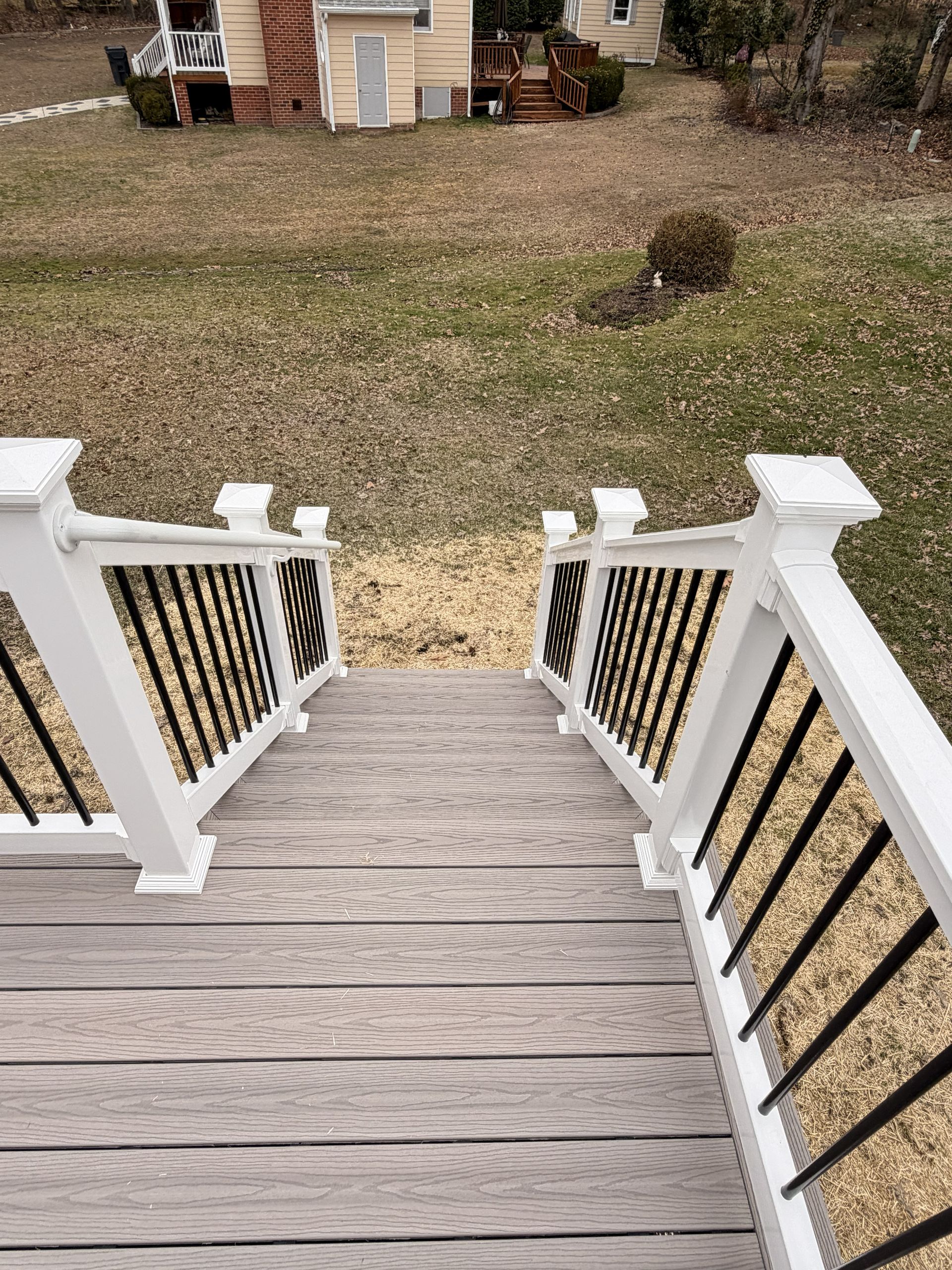 Front porch steps with white railings leading to a winter yard and a small shed in the distance.
