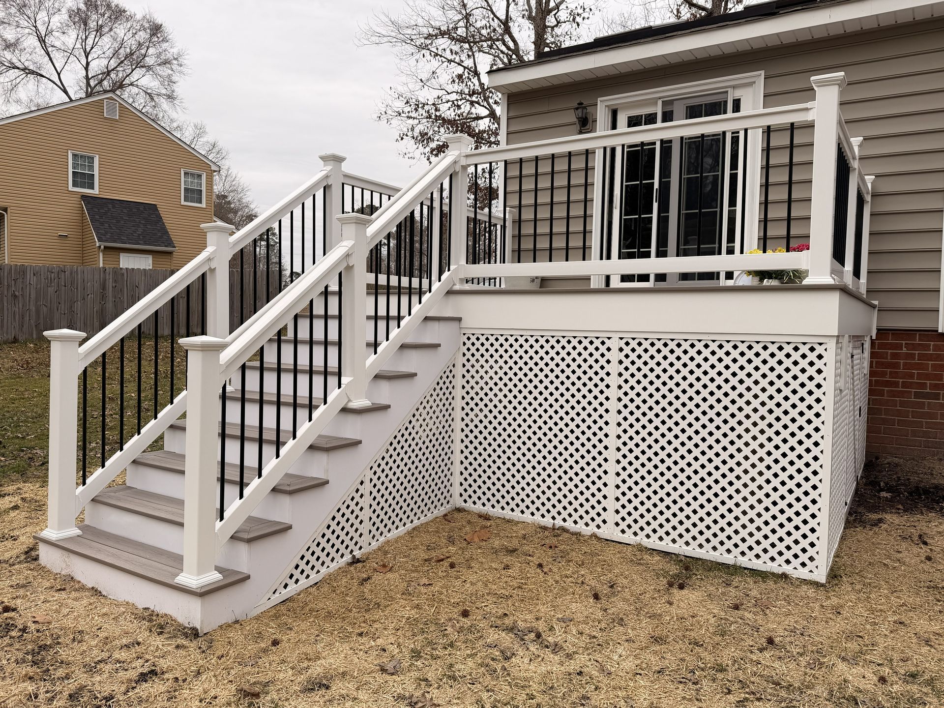 White wooden deck stairs with railing on a house, bordered by white lattice skirting
