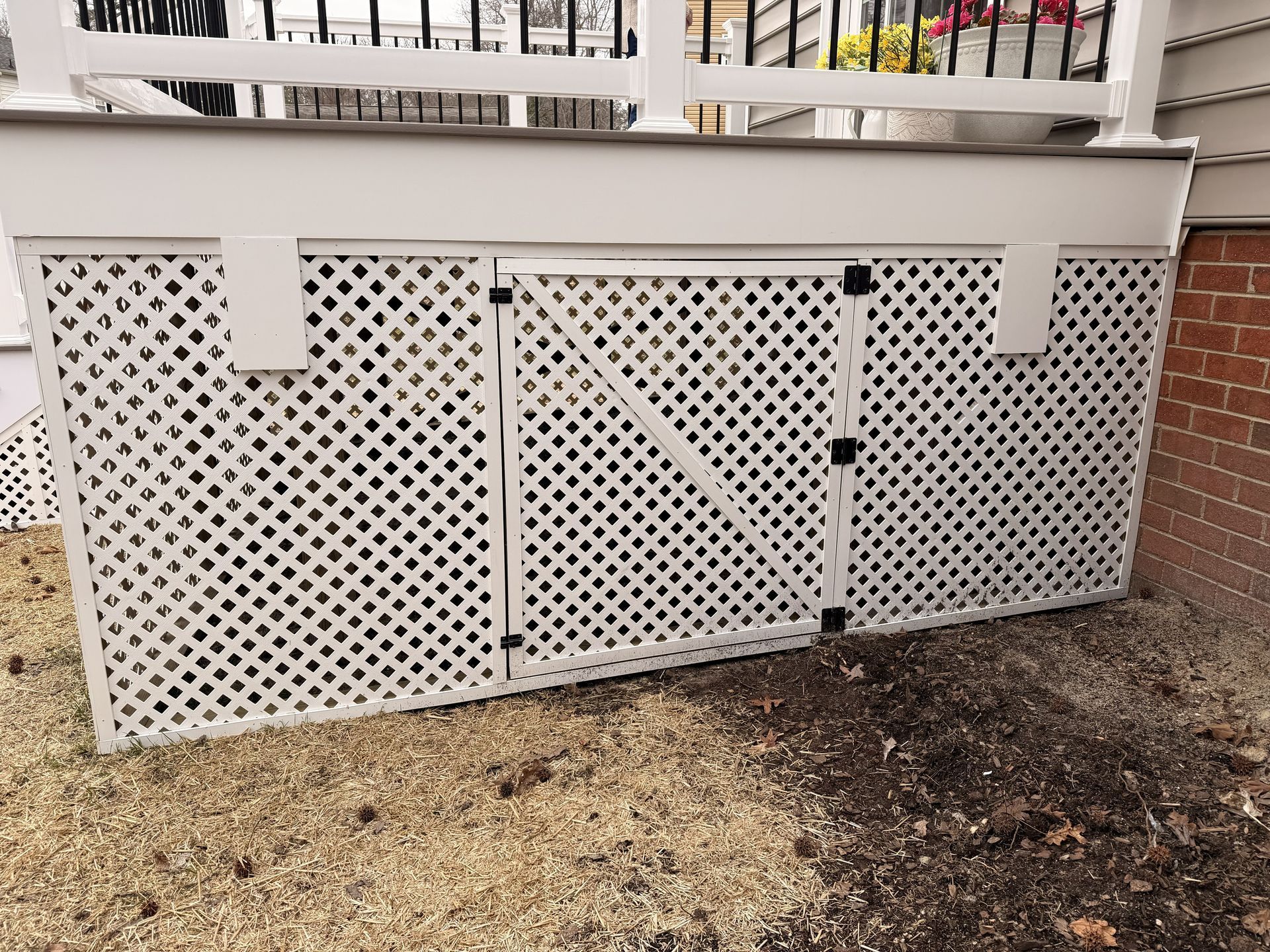 White lattice deck skirt with access door under a porch, beside a gravel and dirt yard.