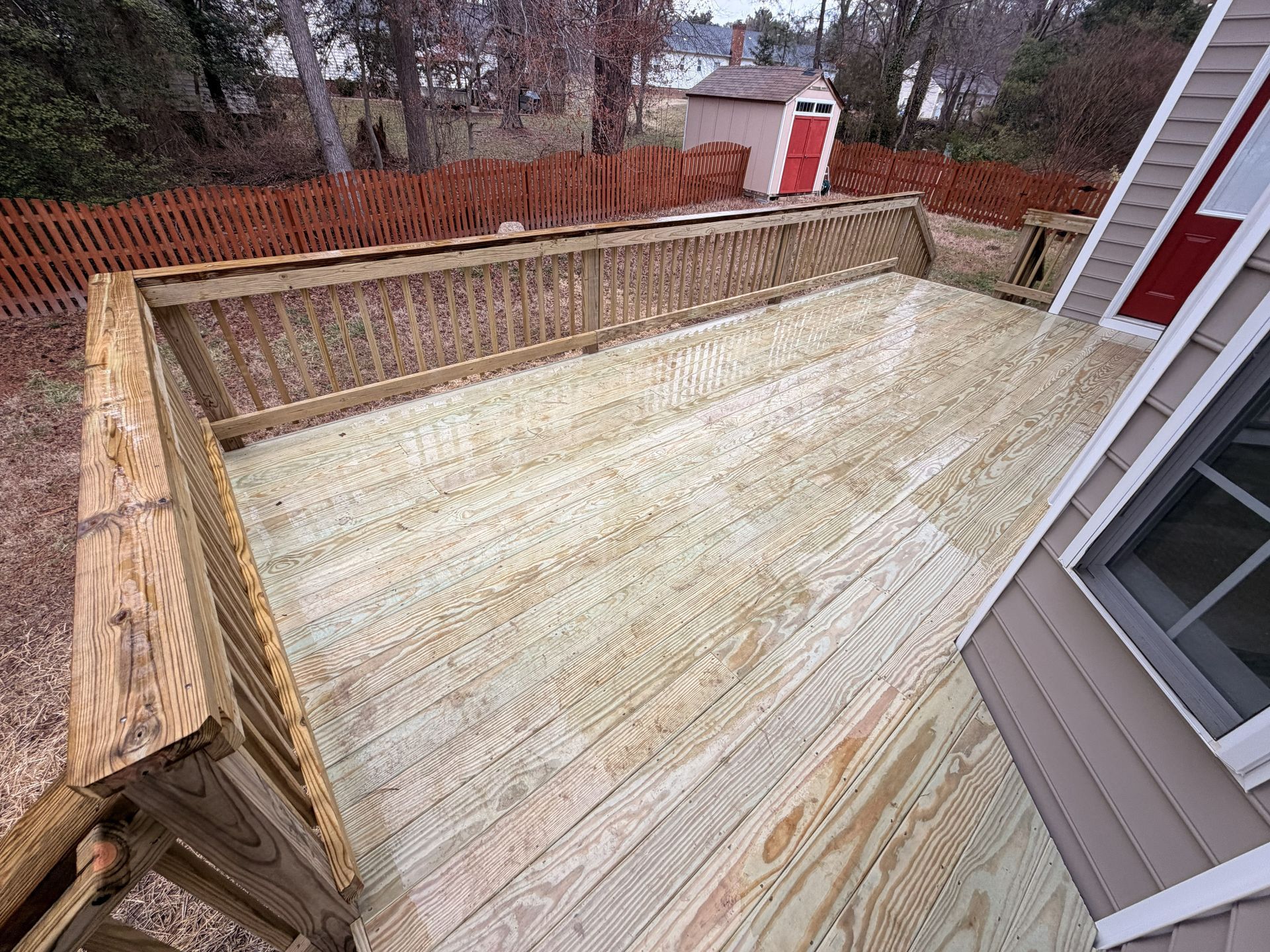Wooden backyard deck under construction, viewed from above, with railings and house siding visible.