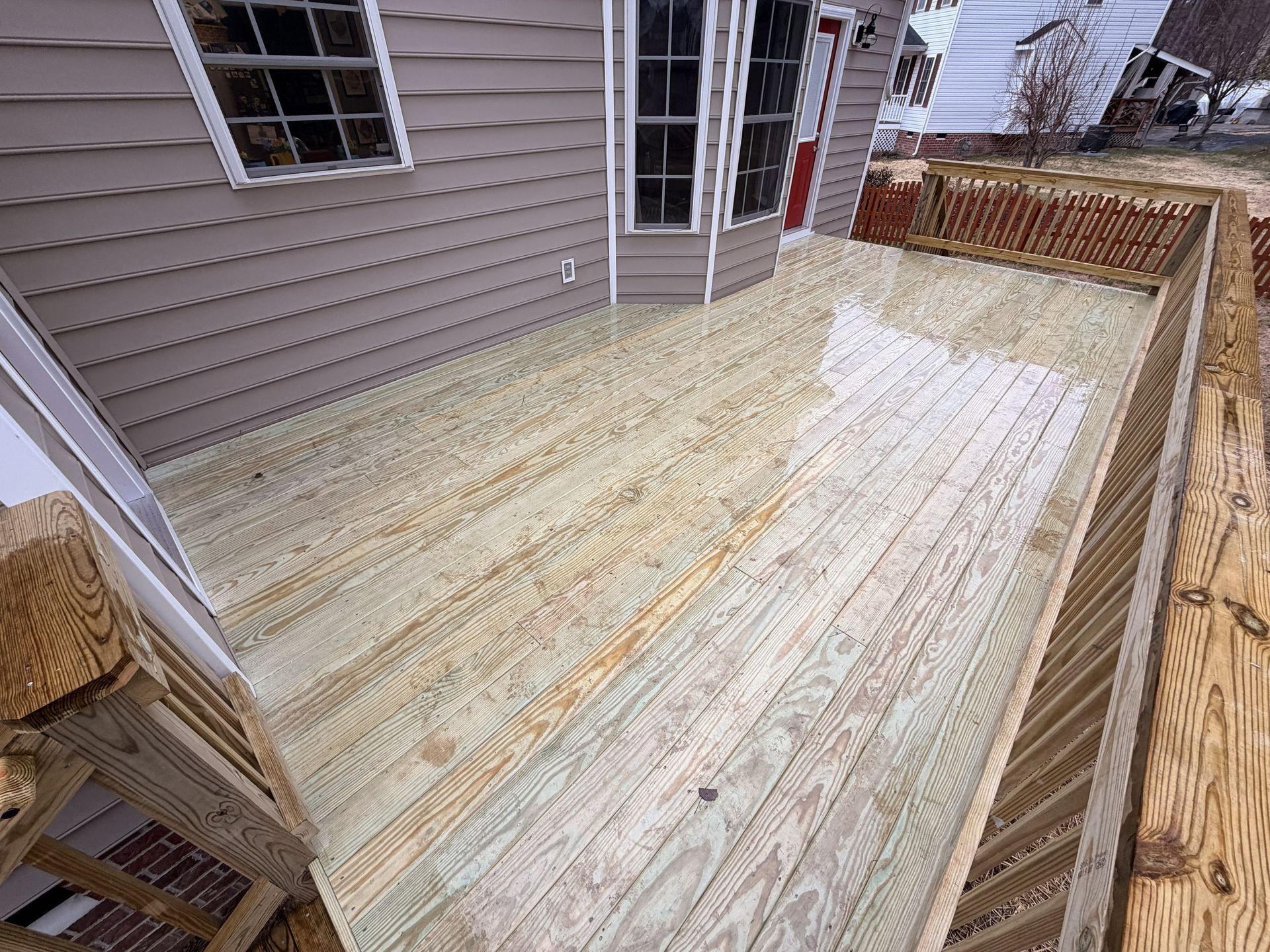 Wooden deck beside a house with pale siding and a fenced yard area, viewed from above