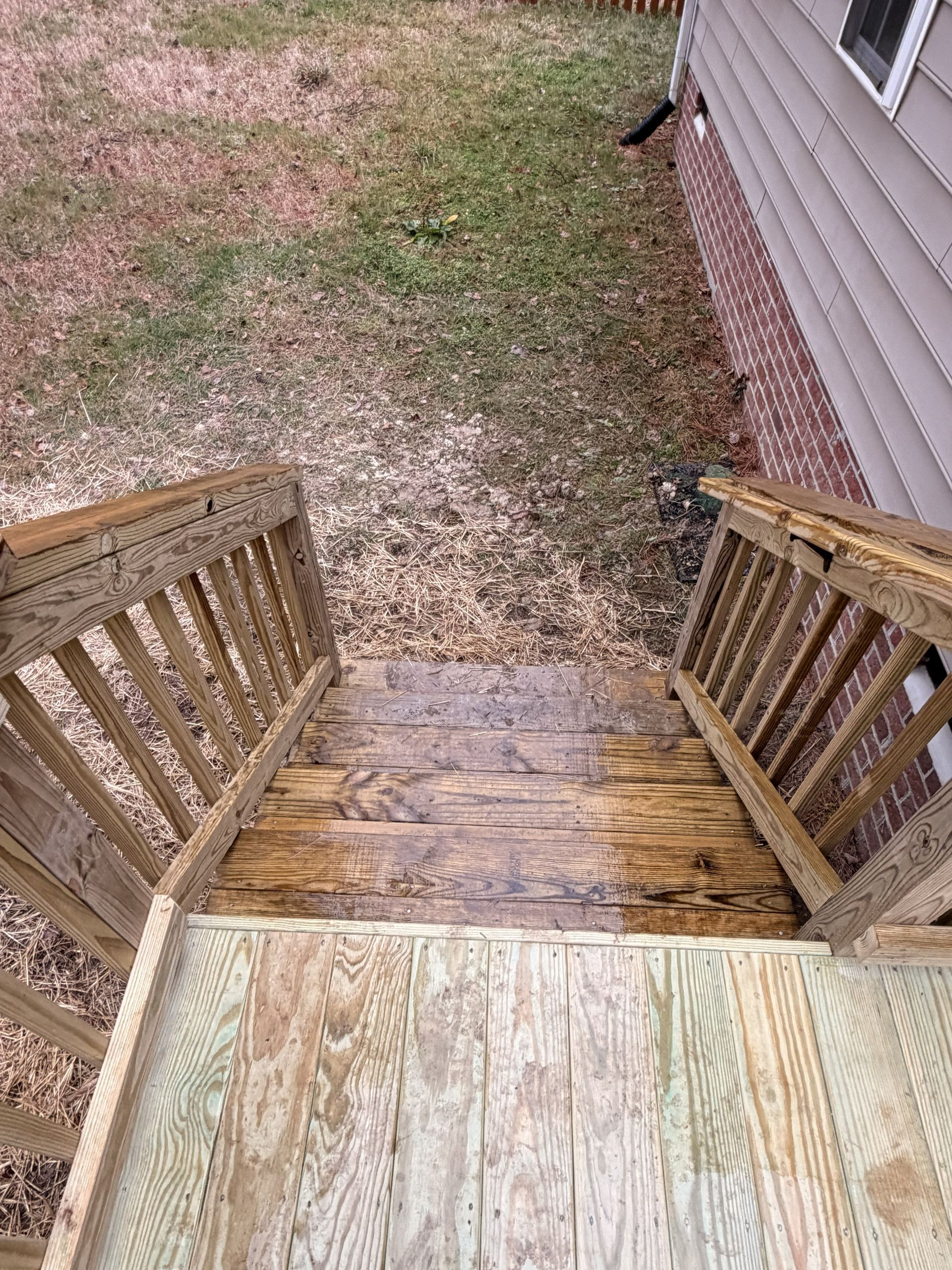Wooden deck steps descending to a patchy backyard beside a house with beige siding.