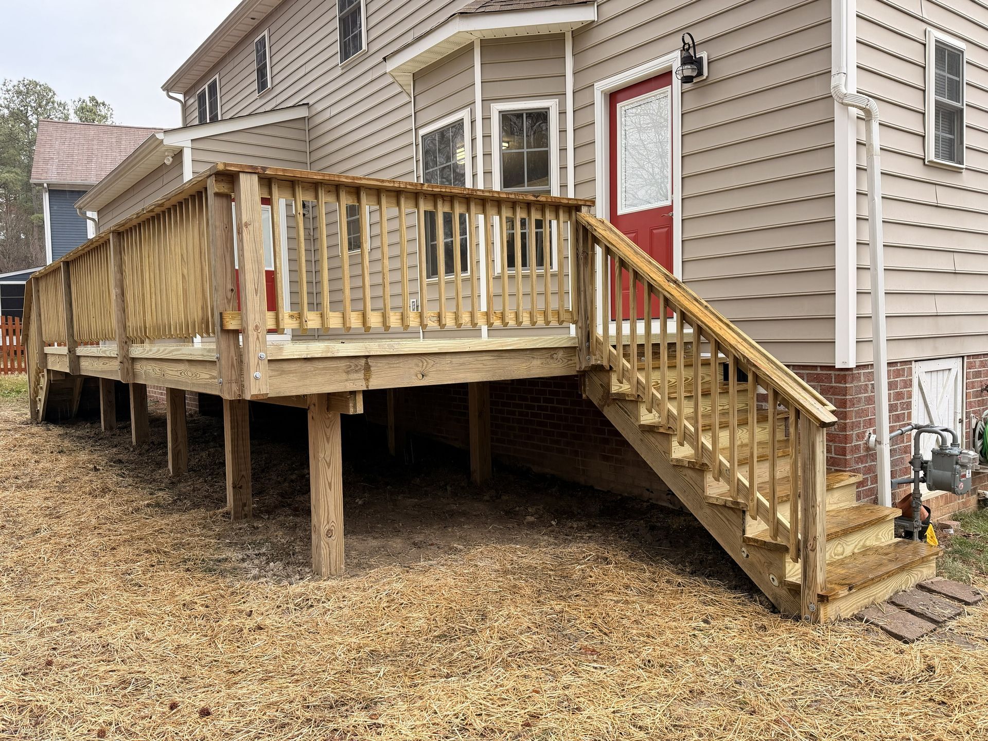 Raised wooden deck and stairs attached to a beige house on concrete posts.
