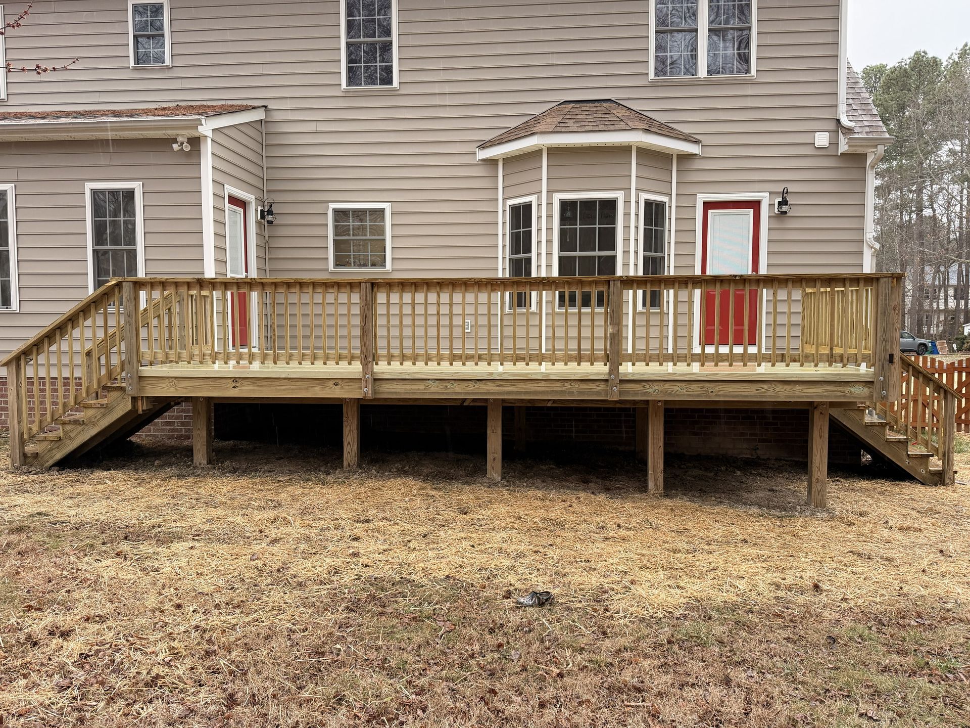 Wooden backyard deck with railing and steps attached to a beige house