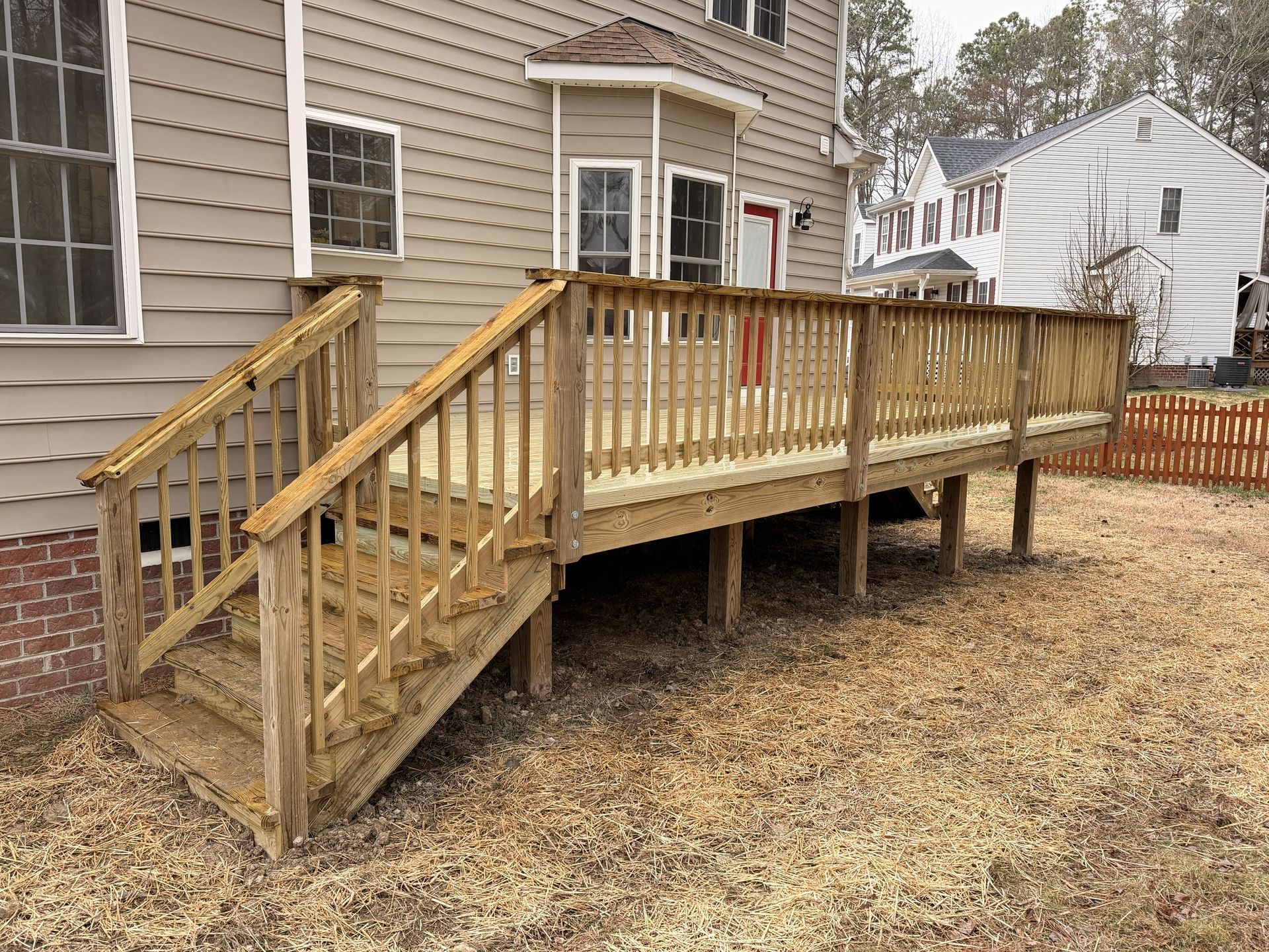 Wooden accessibility ramp and stairs attached to a gray house with a red door.