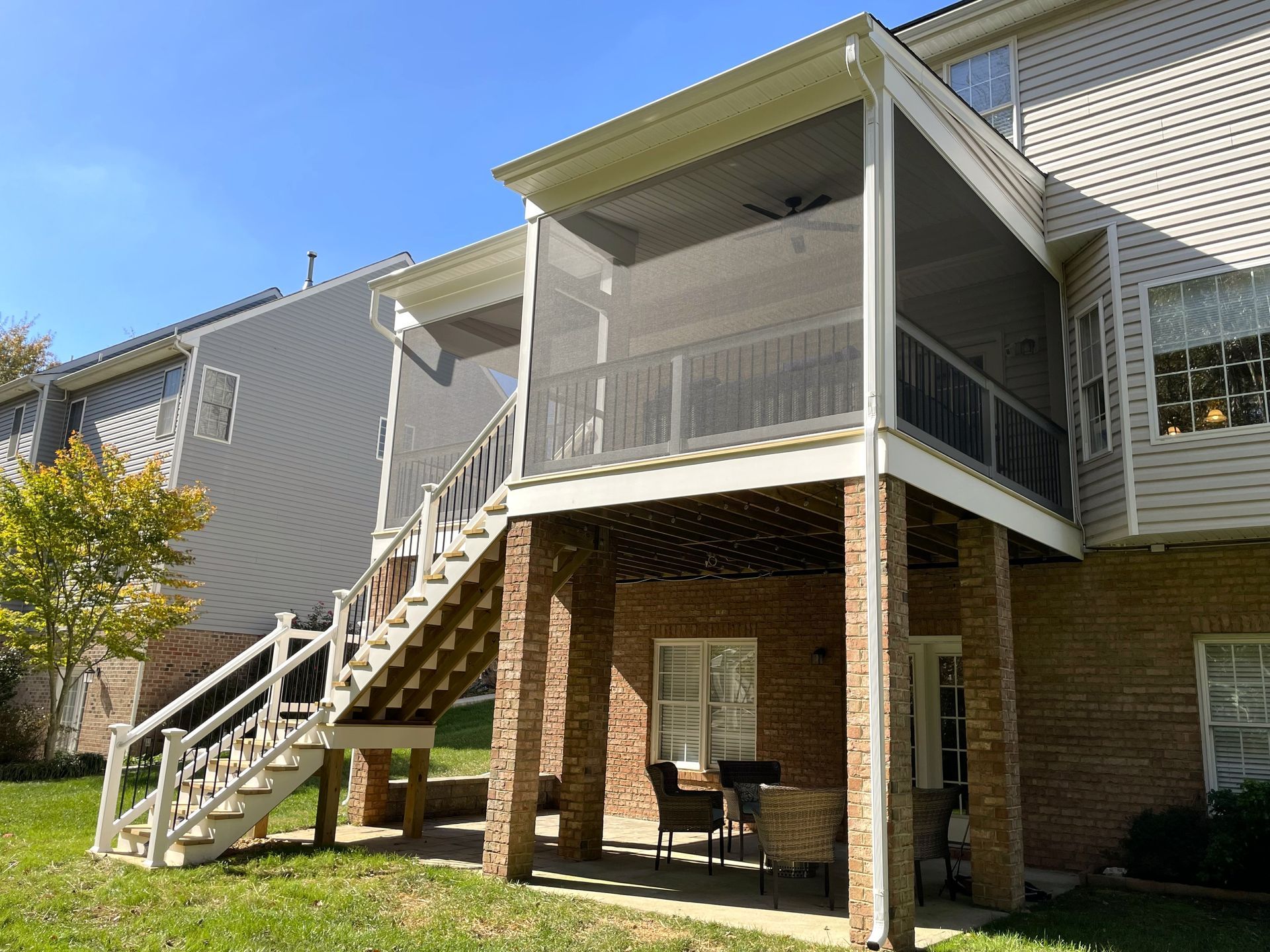 Apartment exterior with white stairway, screened porch, and brick patio below under blue sky
